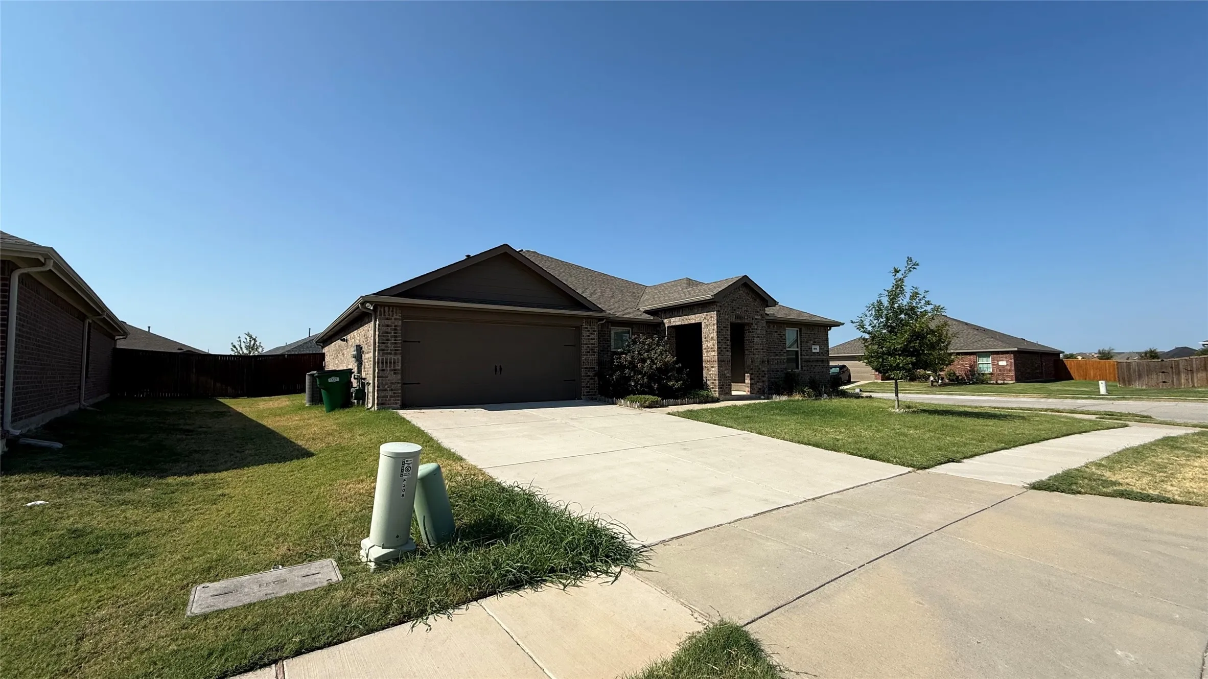 Brick exterior with an attached two-car garage, concrete driveway, and a front lawn with a single tree