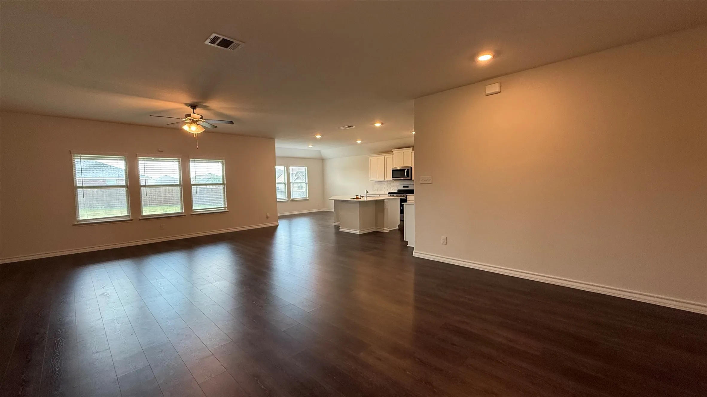 Expansive open-concept living area featuring dark wood-finish flooring, recessed lighting, and a ceiling fan