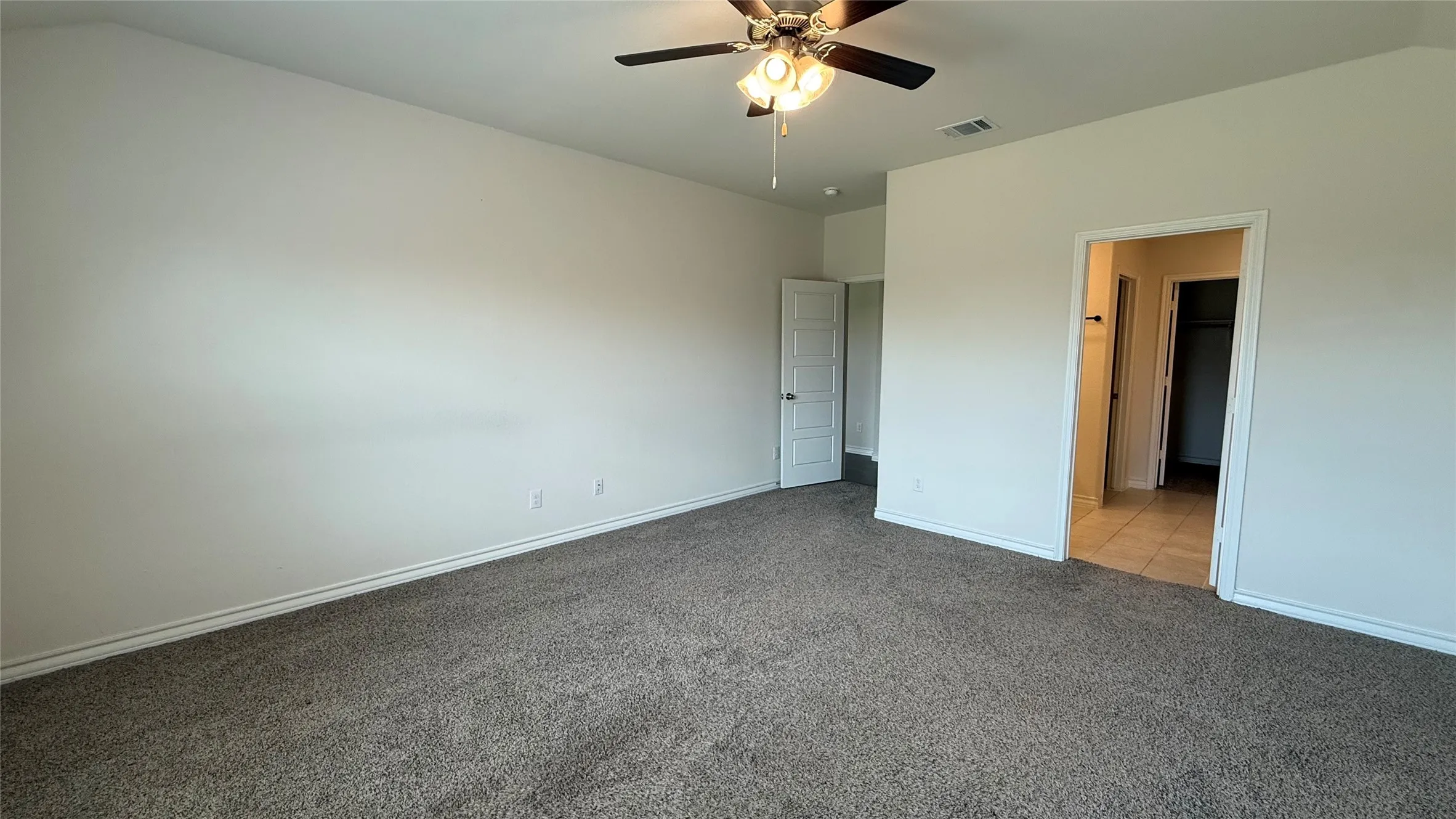 Neutral tone wall paint, textured carpet flooring, ceiling fan with integrated lighting, and interior doorways