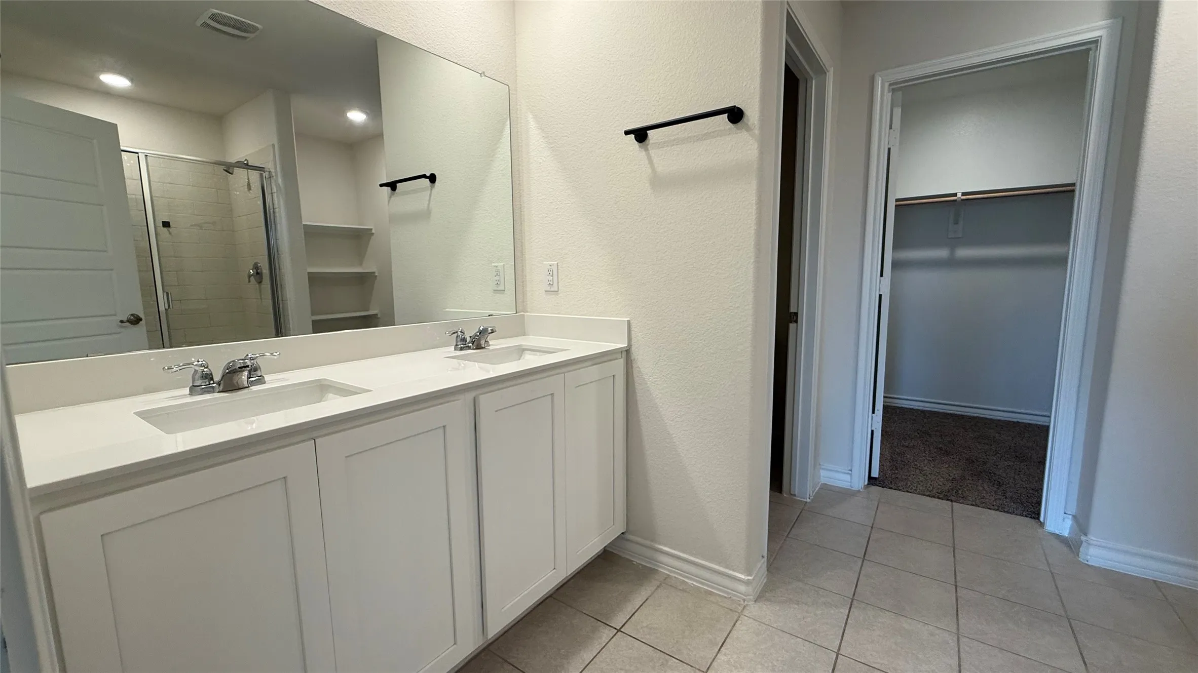 Double vanity with white cabinetry and integrated sinks, a framed mirror, and a glass-enclosed shower with tile surround