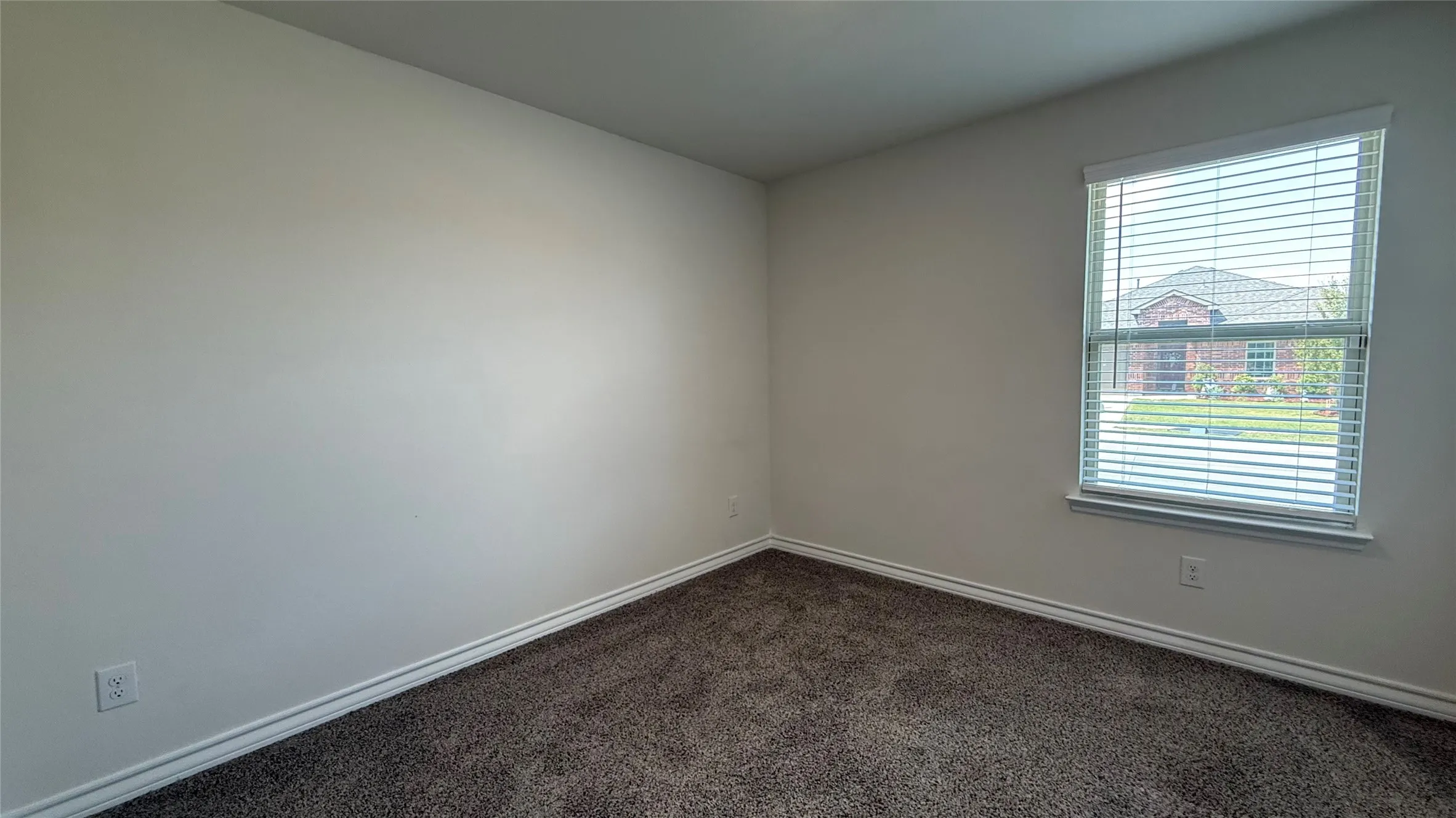 Neutral wall paint, textured carpeting, window with blinds, and white trim