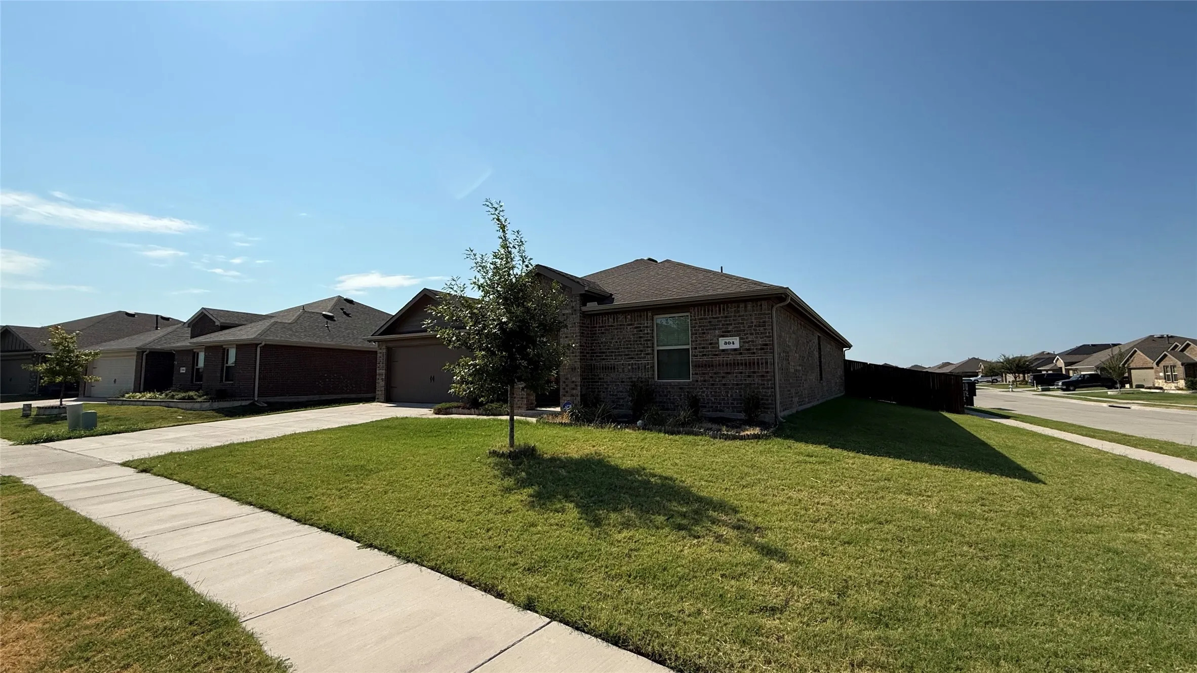 Brick-clad exterior with a dark-shingle roof, concrete driveway, and front lawn