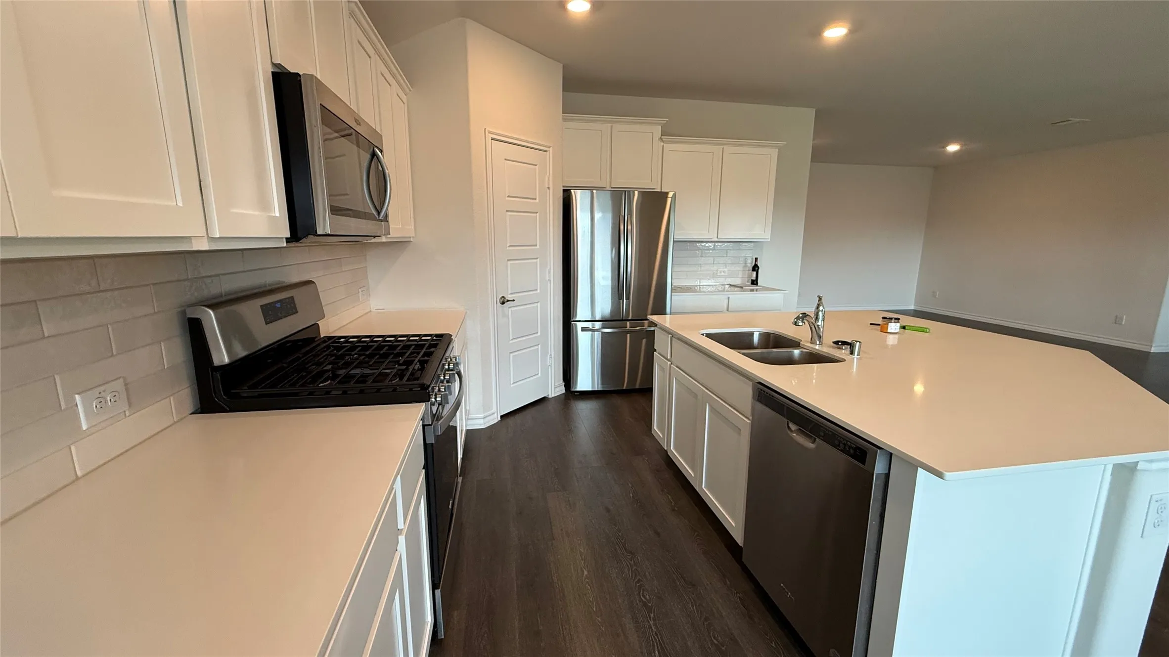 Contemporary kitchen featuring white cabinetry, light countertops, subway tile backsplash, and stainless steel appliances