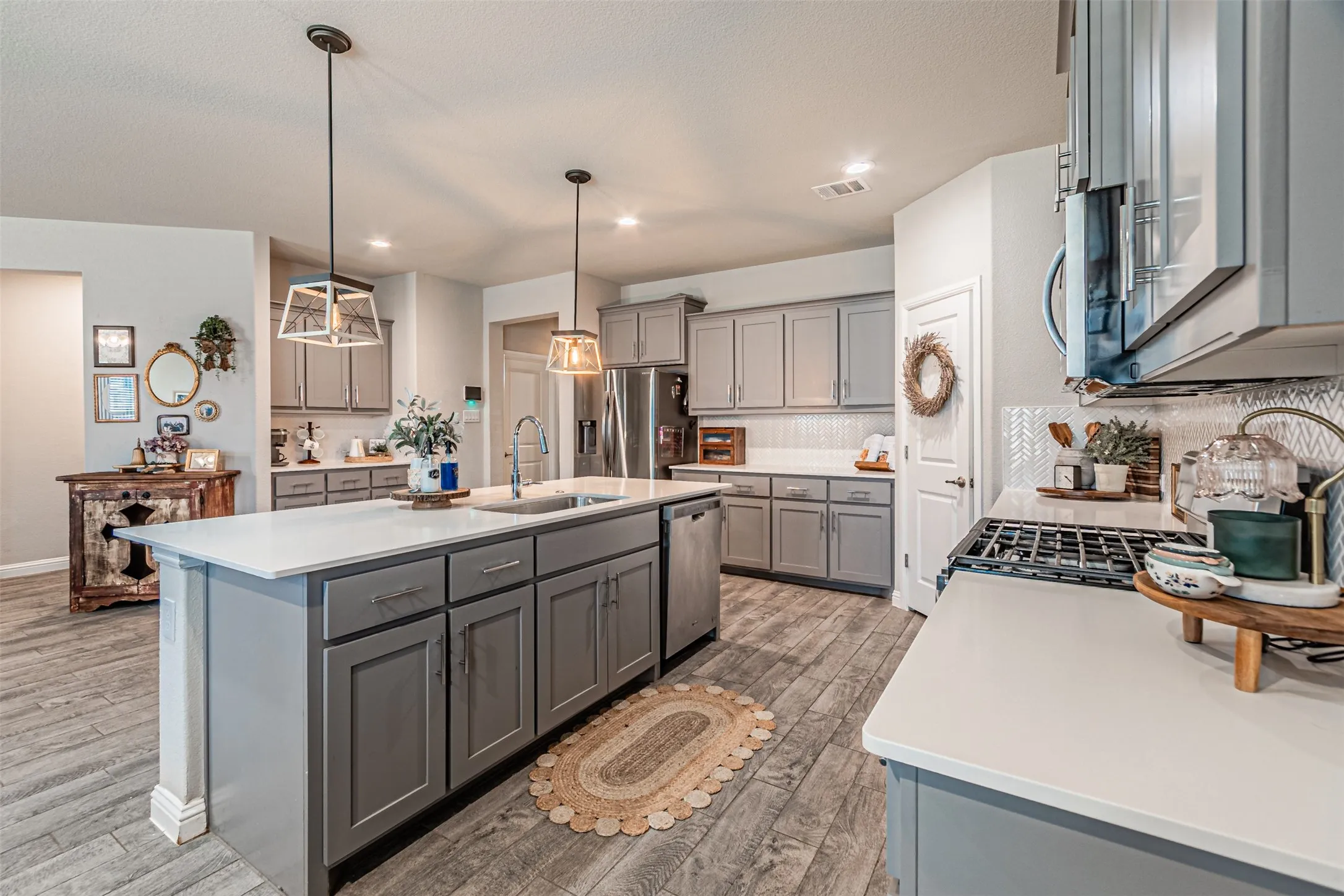 Kitchen featuring light gray cabinetry, white countertops, stainless steel appliances, wood-finish flooring, and pendant lighting