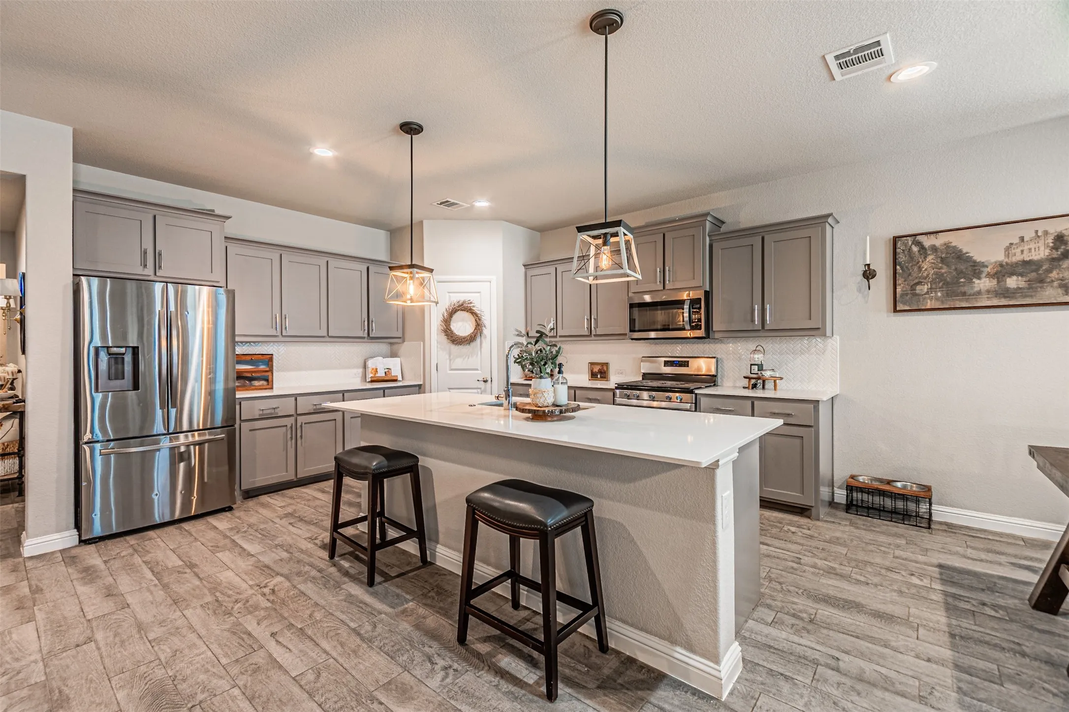 Kitchen featuring grey cabinetry, stainless steel appliances, wood-finish flooring, a central island with a solid surface countertop, and recessed lighting