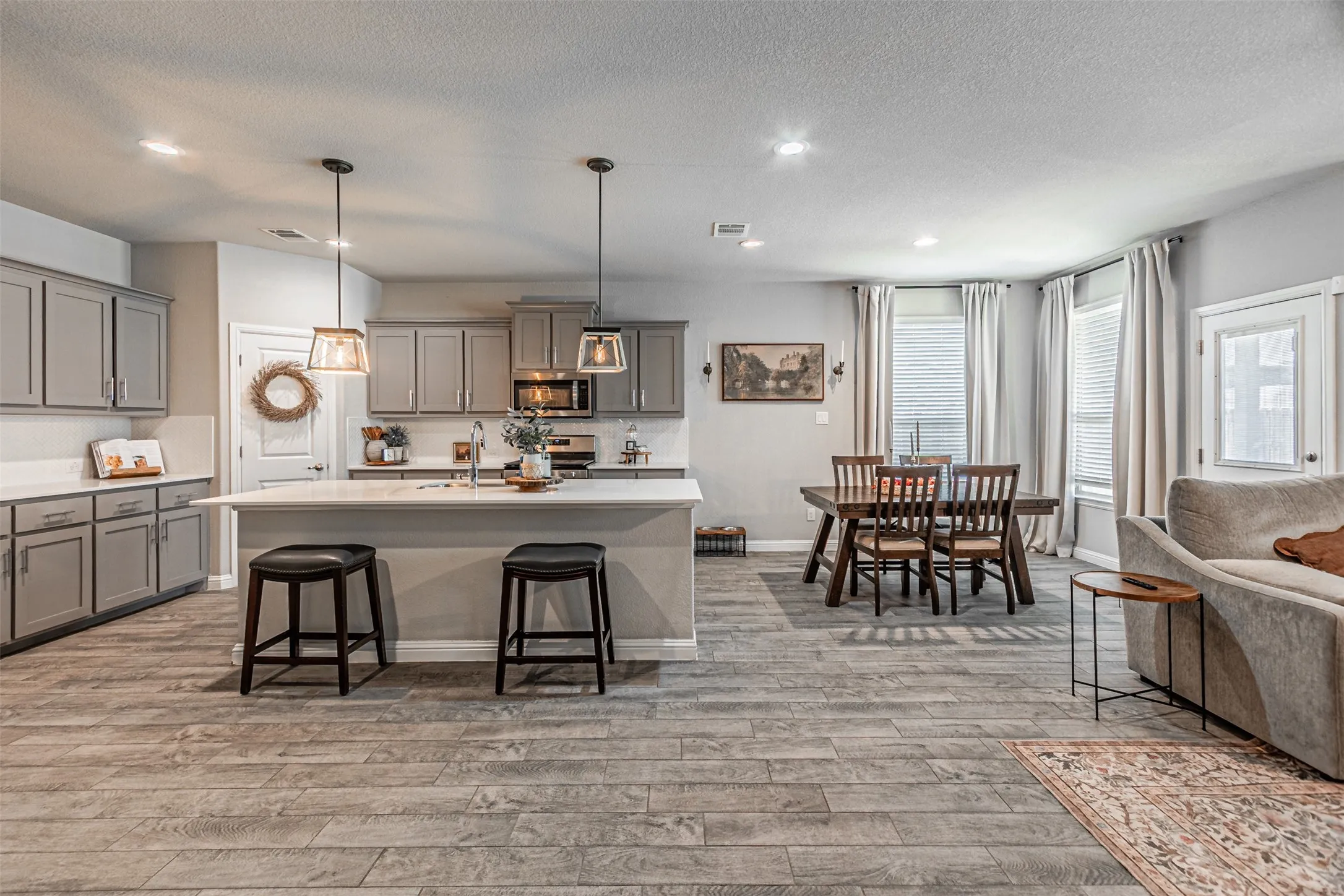 Open-concept living area with wood-finish flooring, a kitchen island, pendant lighting, built-in cabinetry, and integrated appliances