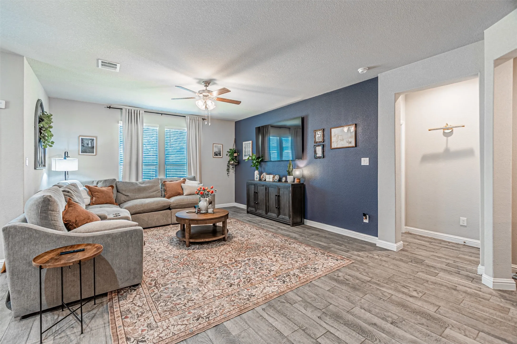 Spacious living area featuring wood-finish flooring, a ceiling fan, and a dedicated accent wall