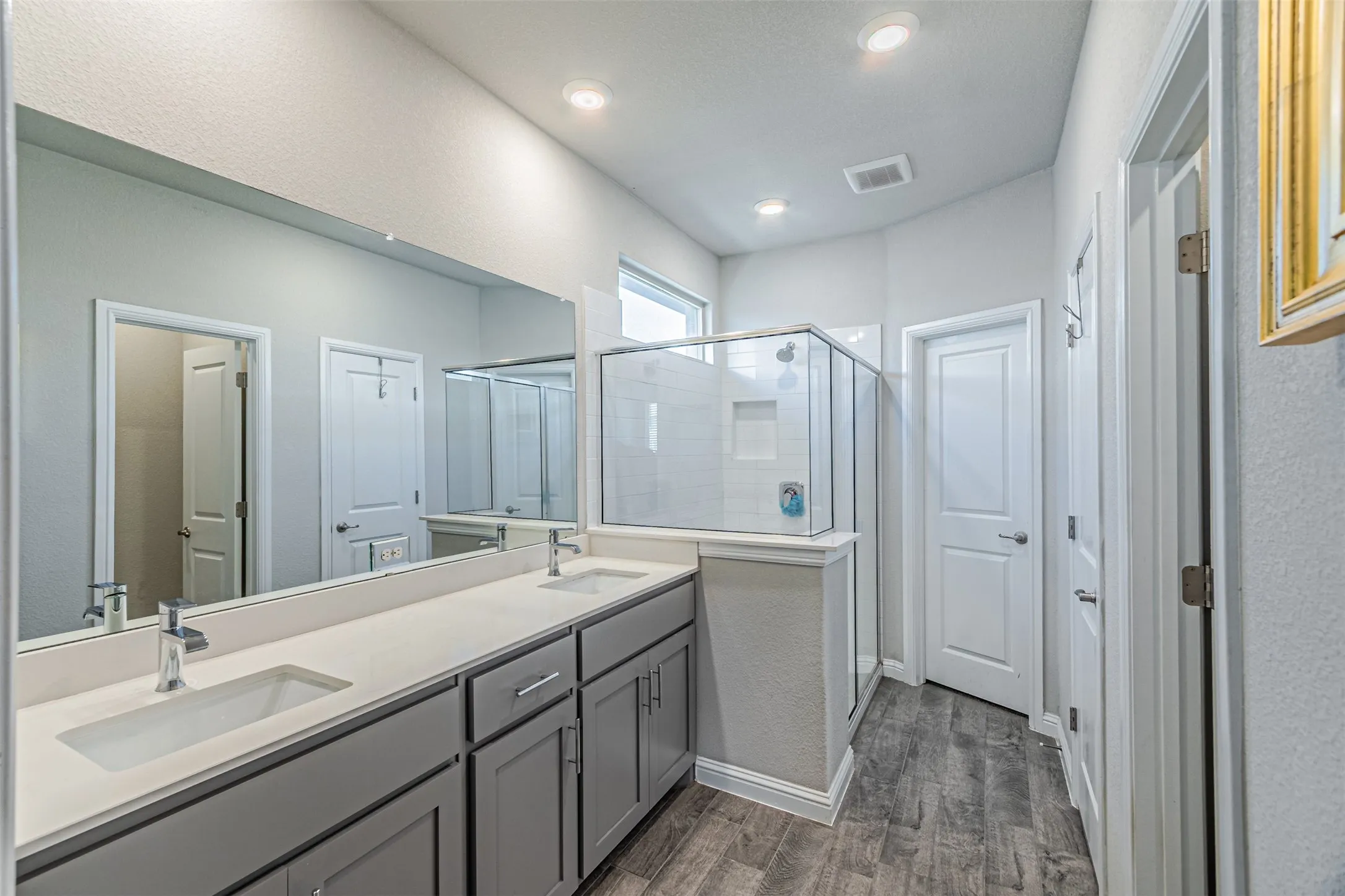 Dual vanity with undermount sinks, wood-finish flooring, glass-enclosed shower, built-in storage, and recessed lighting