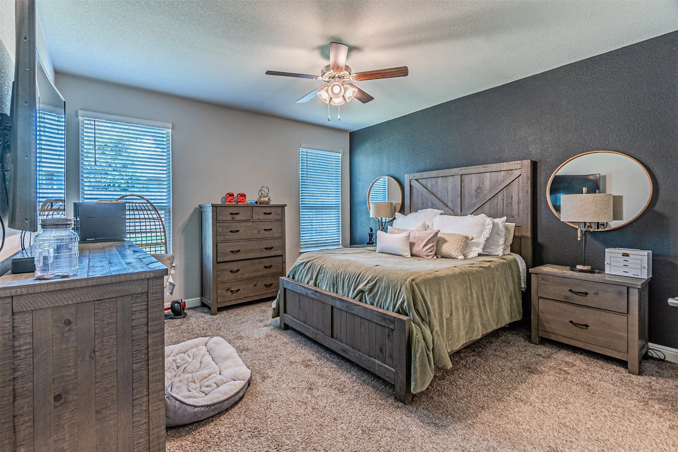 Carpeted flooring, ceiling fan with integrated lighting, multiple windows with blinds, and an accent wall