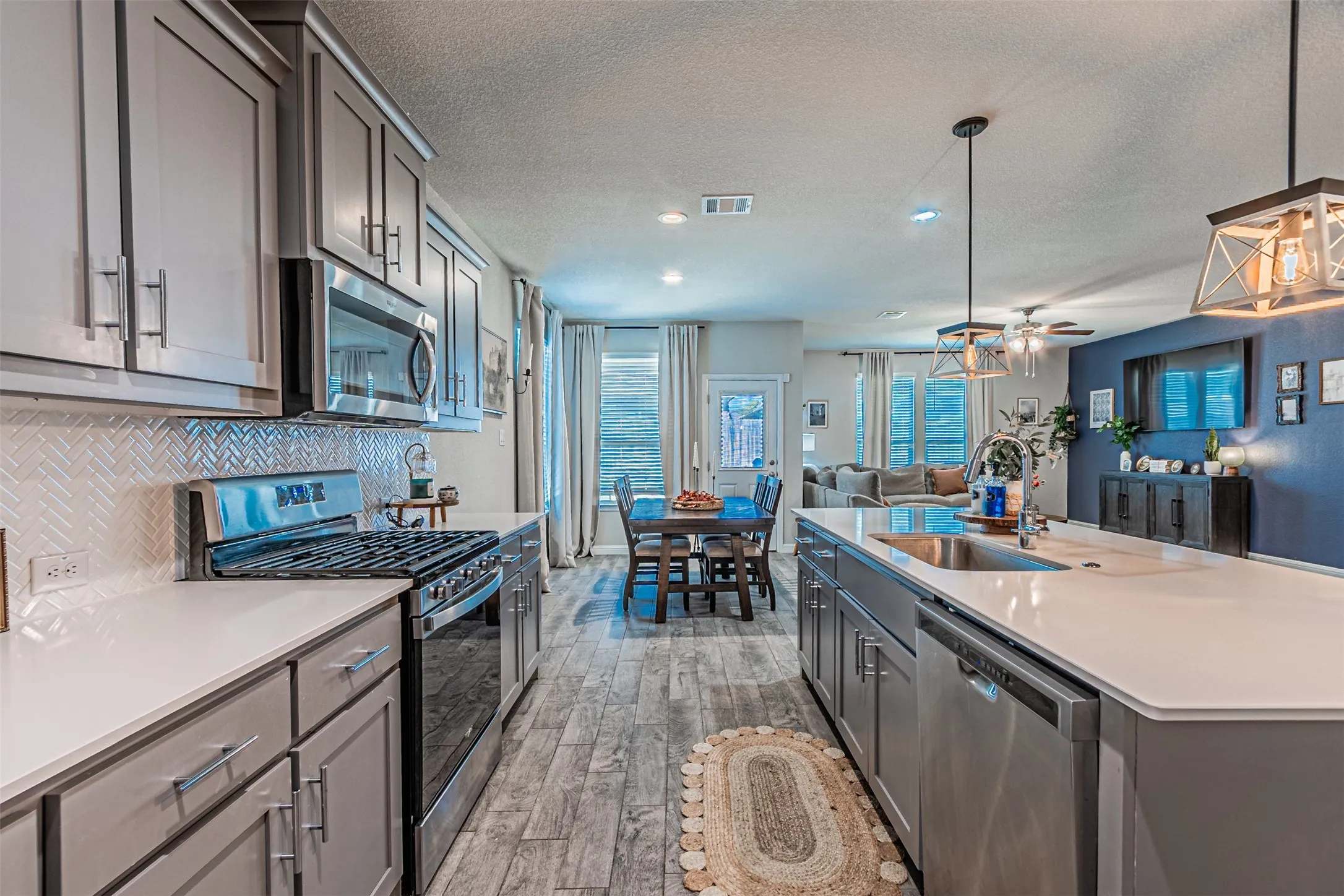 Kitchen featuring stainless steel appliances, light gray cabinetry, white countertops, and a herringbone tile backsplash