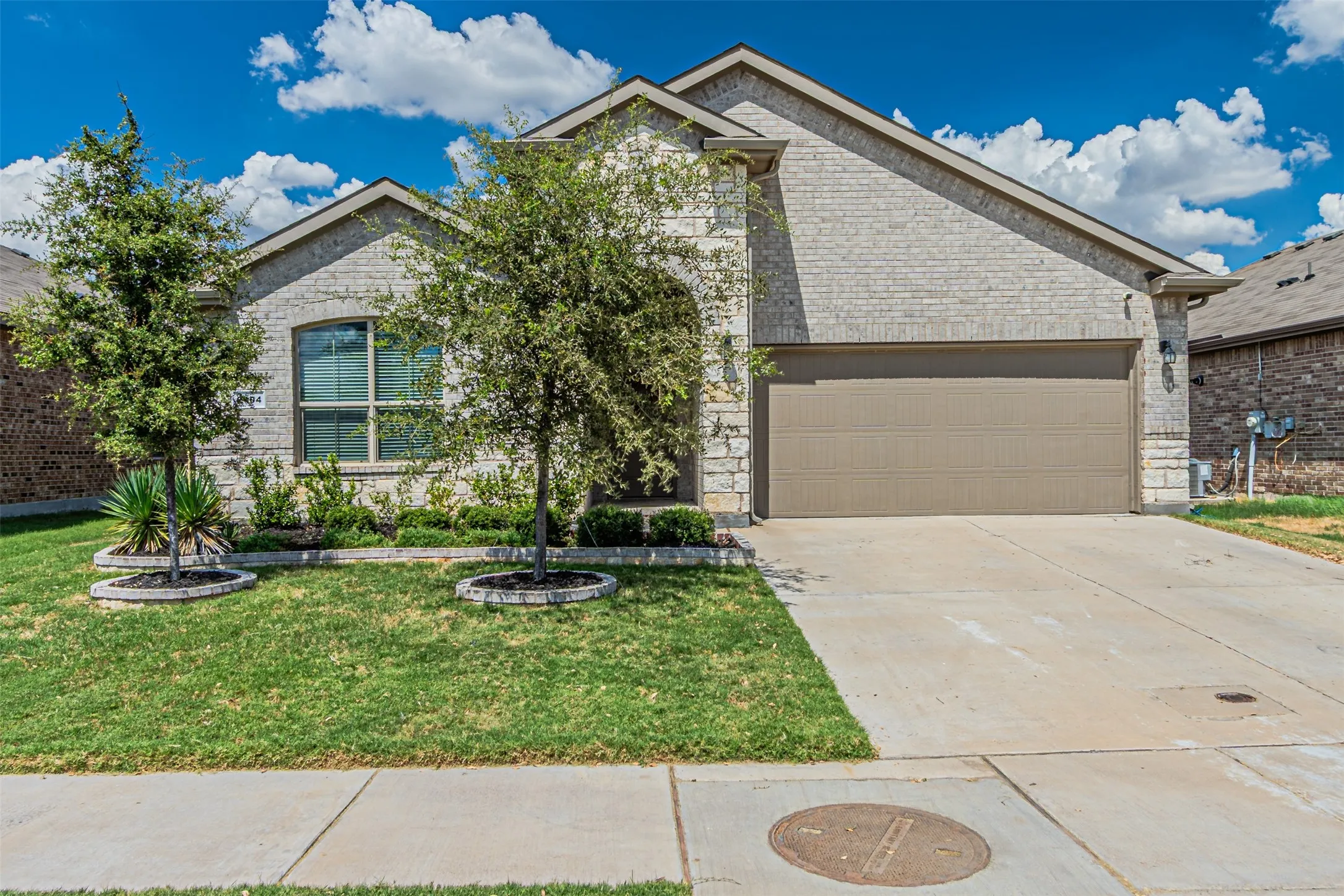 Brick and stone exterior with a two-car garage, concrete driveway, and landscaped front yard