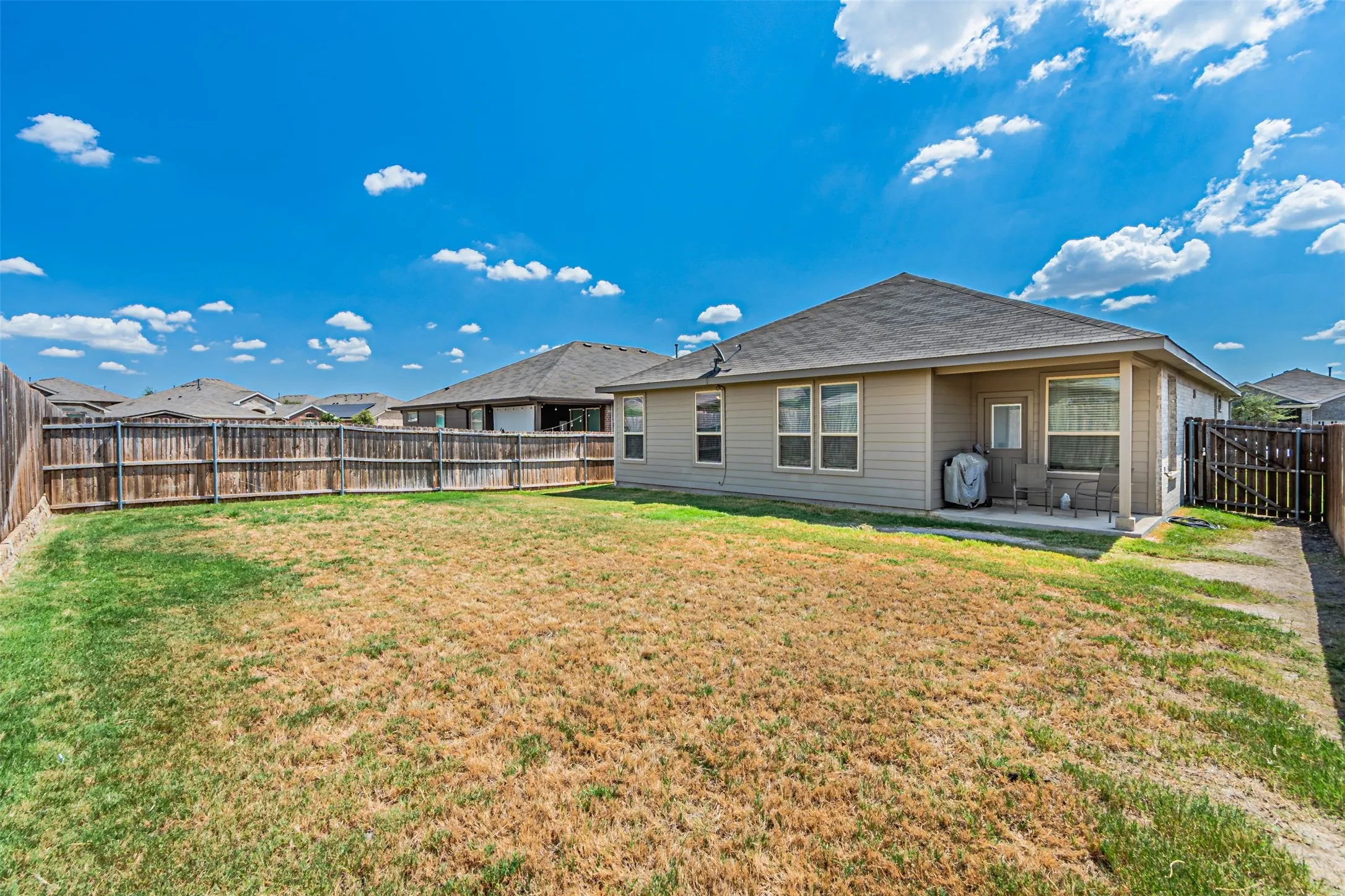 Expansive rear yard with wood privacy fencing, a concrete patio, and a covered patio area