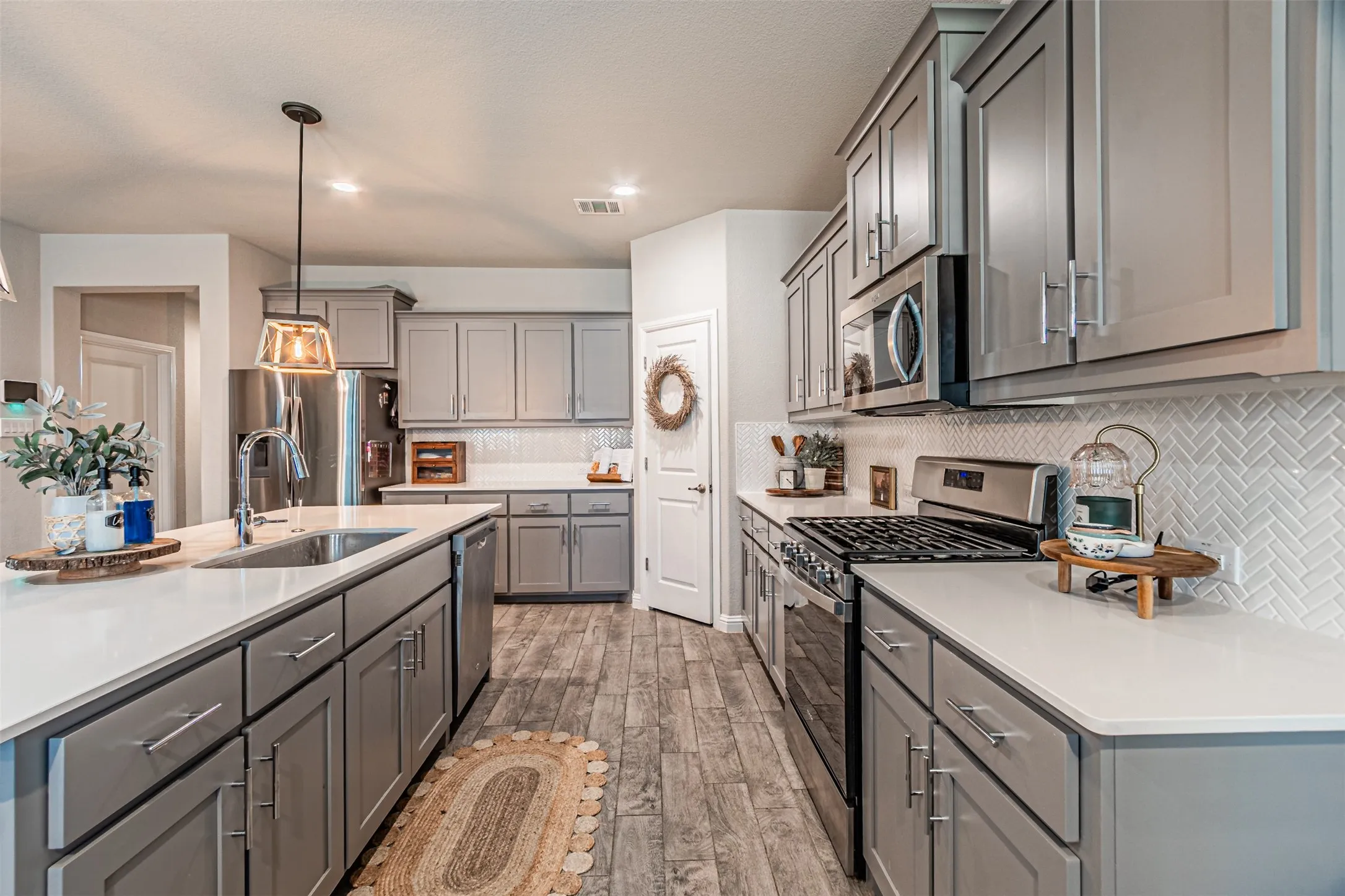 Well-appointed kitchen featuring gray cabinetry, stainless steel appliances, white countertops, a herringbone tile backsplash, and wood-finish flooring