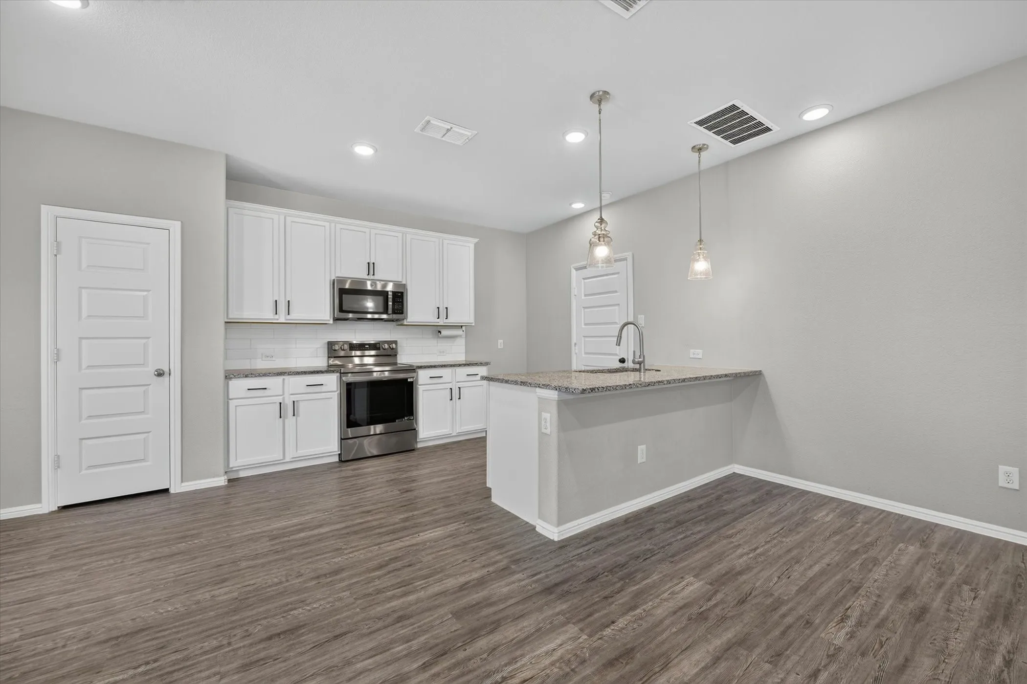 Kitchen featuring white cabinetry, stainless steel appliances, a tile backsplash, wood-finish flooring, and a peninsula with pendant lighting