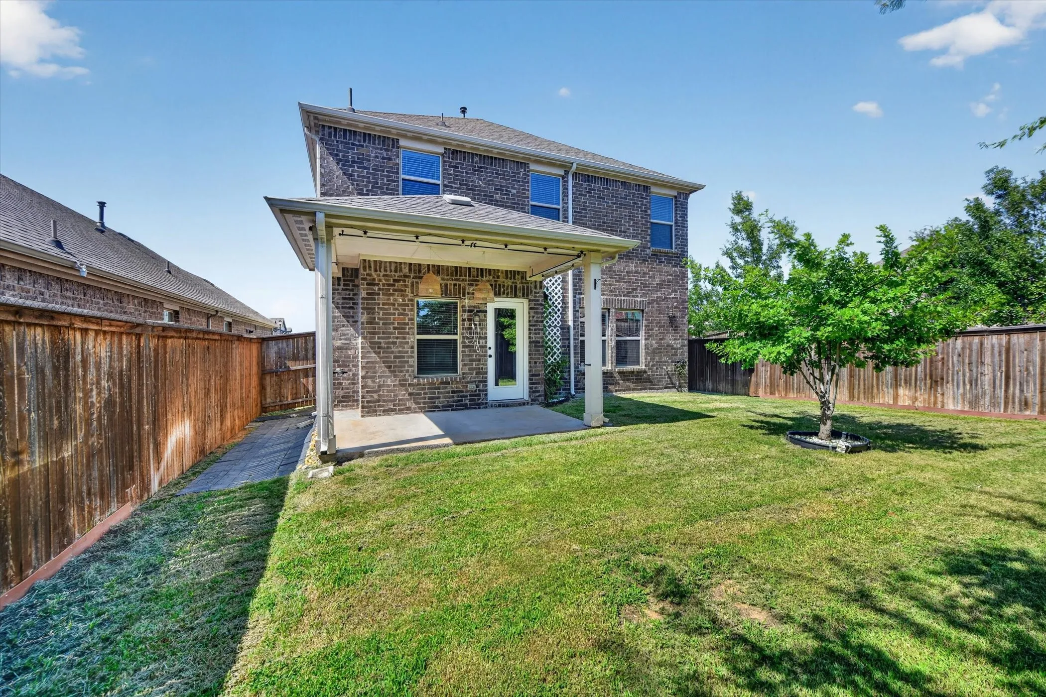 Expansive backyard featuring a covered patio, brick exterior, and a mature tree