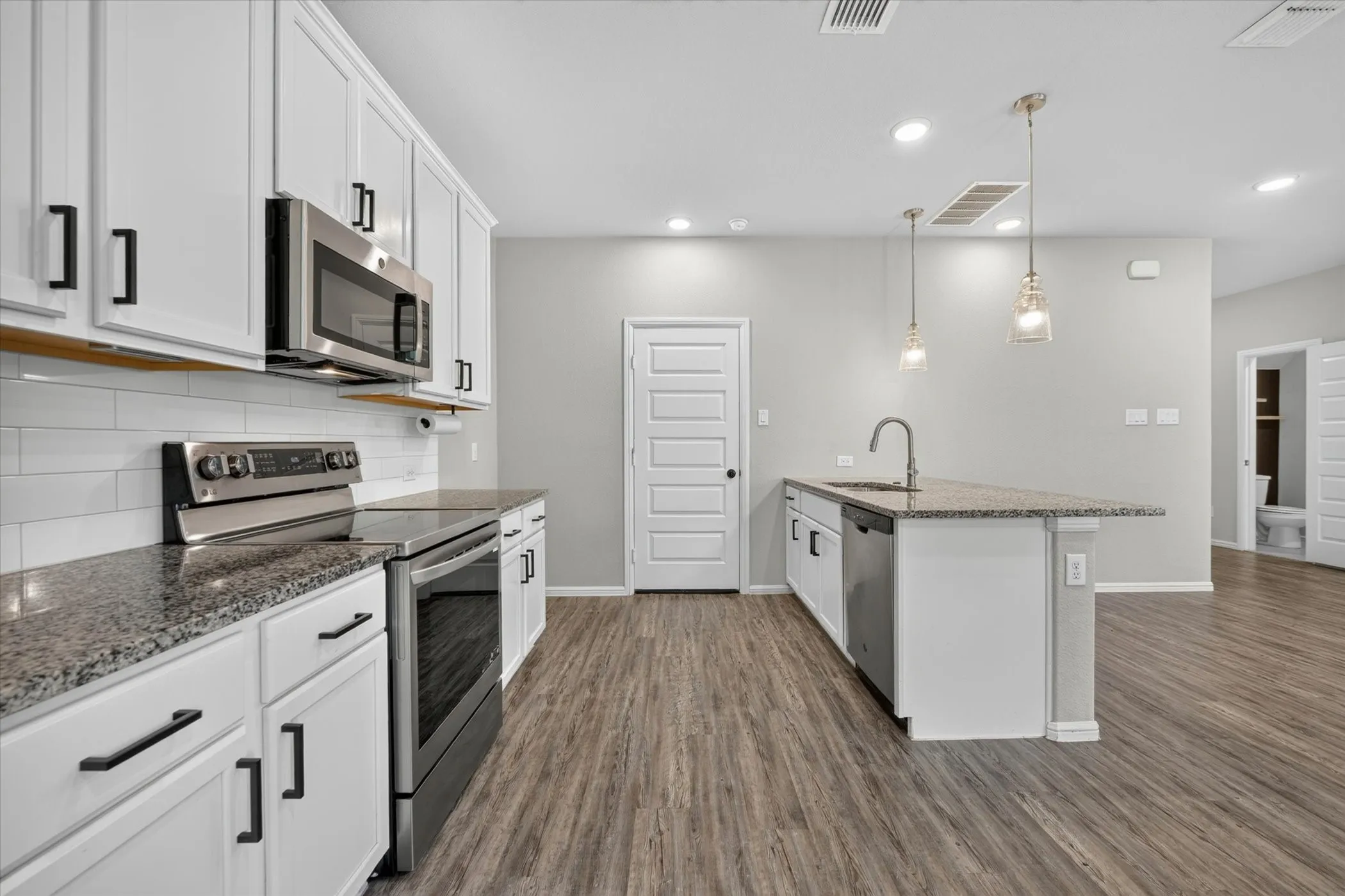 Wood-finish flooring, white cabinetry, stainless steel appliances, recessed lighting, and a glass-paneled exterior door