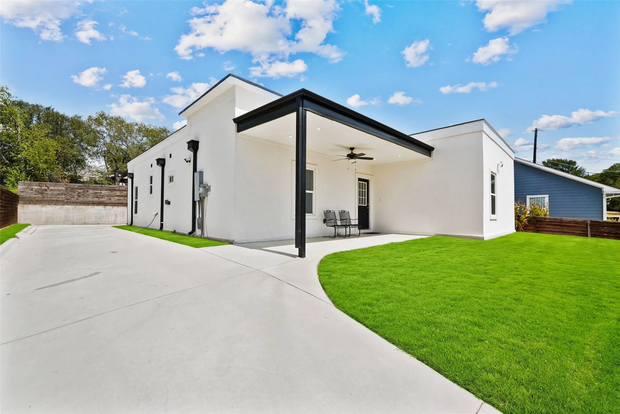 Exterior featuring white facade, a covered patio with a ceiling fan, a concrete driveway, a manicured lawn, and dark trim accents