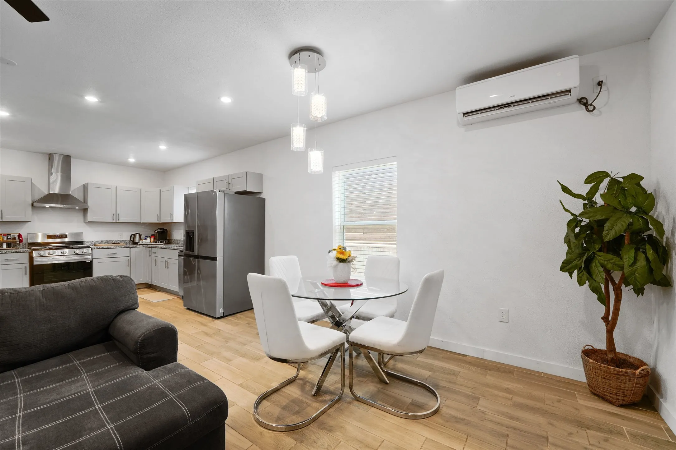 Recessed lighting, wood-finish flooring, stainless steel appliances, light gray cabinetry, and a wall-mounted air conditioning unit