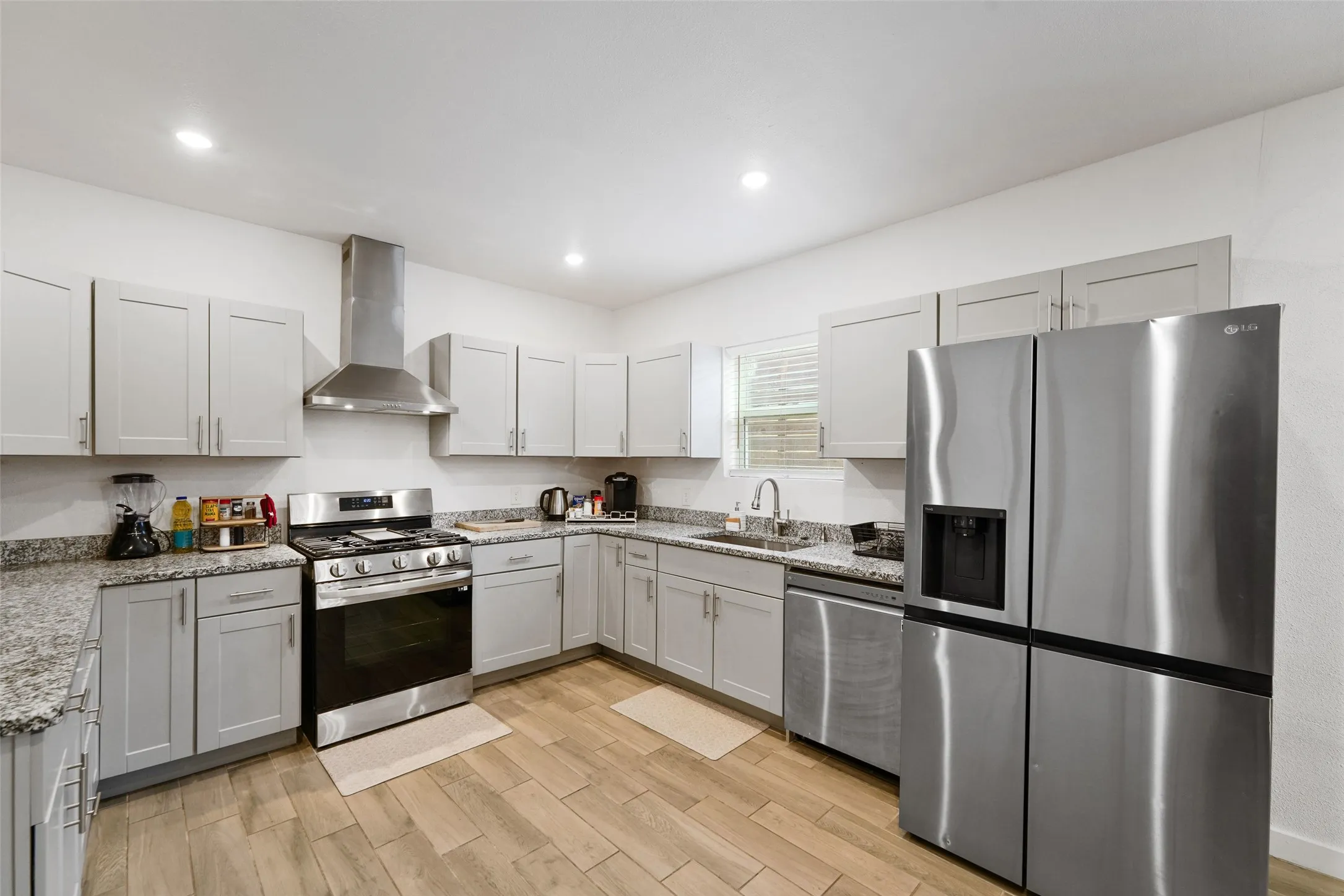 Kitchen featuring light gray cabinetry, granite-style countertops, stainless steel appliances, and wood-finish flooring