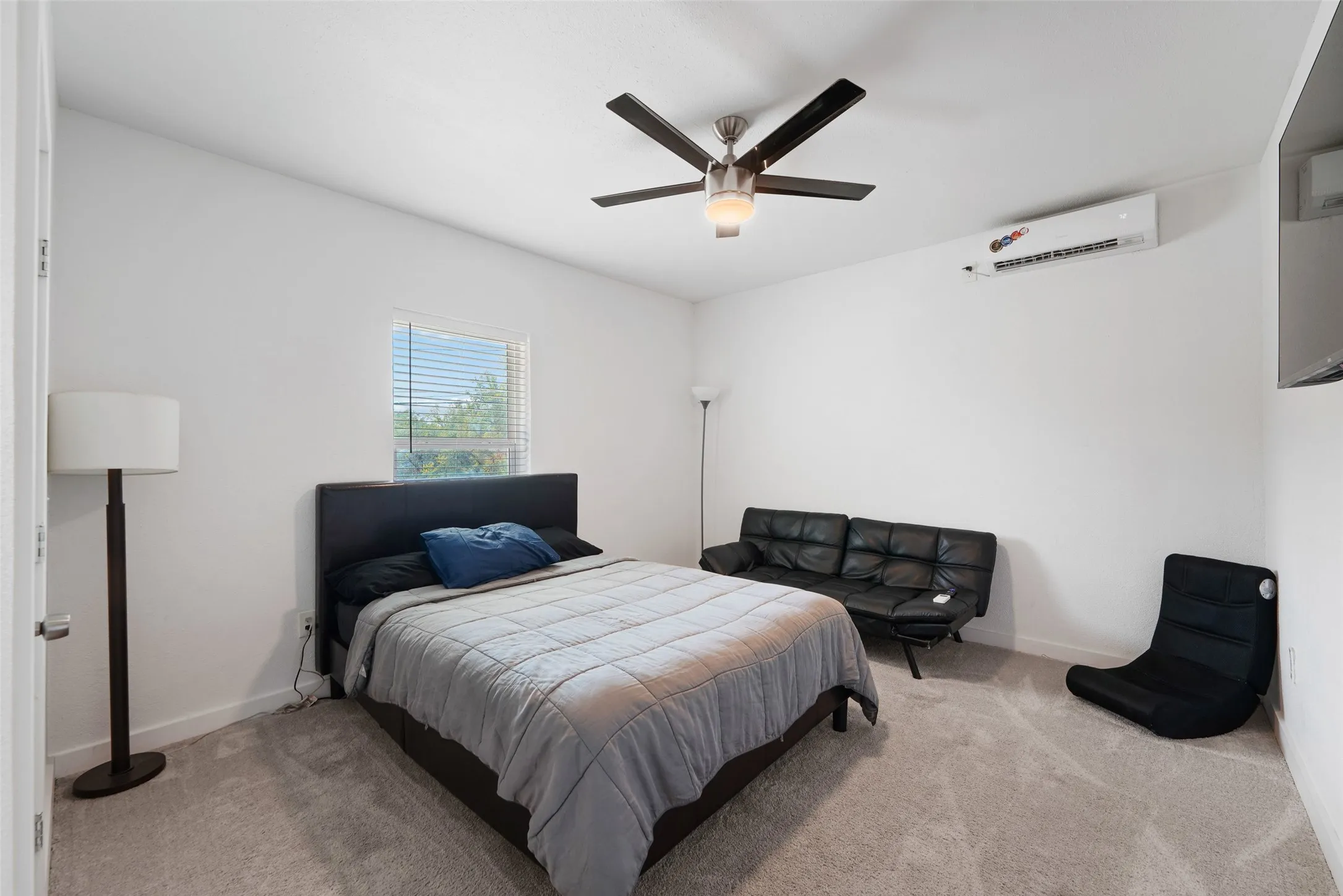 Carpeted room featuring a ceiling fan with integrated lighting, a window with blinds, and a wall-mounted air conditioning unit