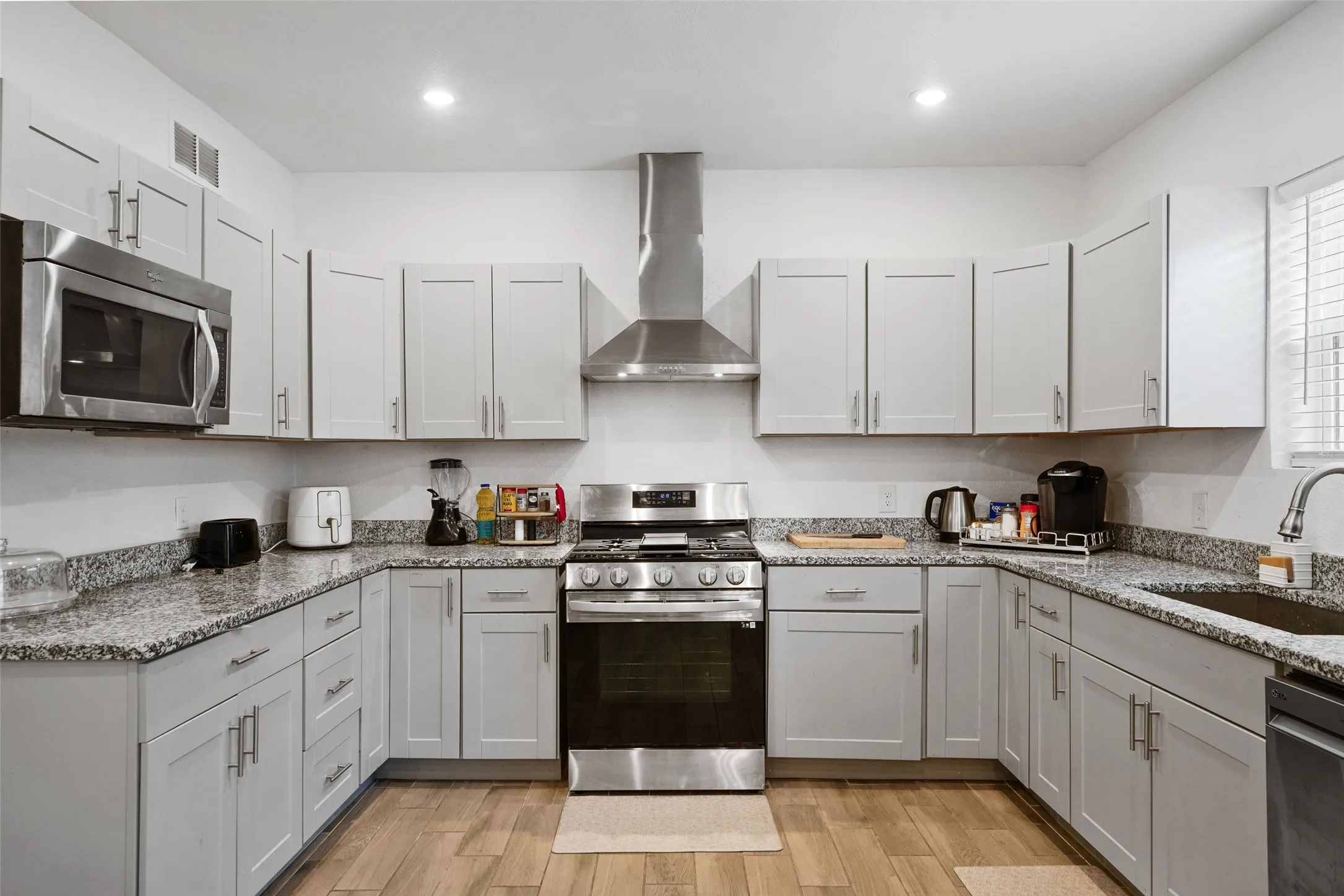 U-shaped kitchen with light-toned cabinetry, stainless steel appliances, speckled stone countertops, and wood-finish flooring