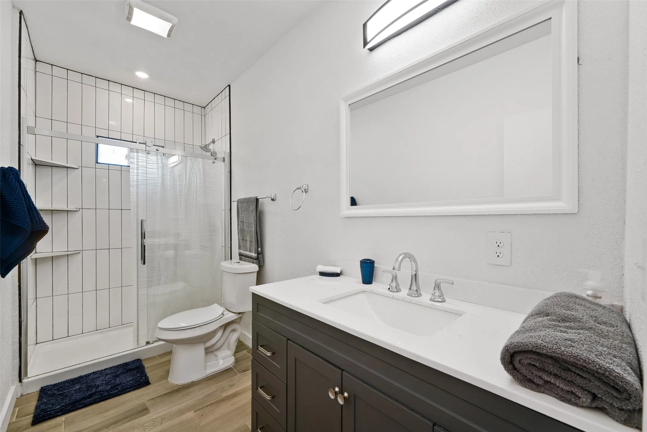Modern bathroom with a dark wood-finish vanity, white countertop, and sleek framed mirror