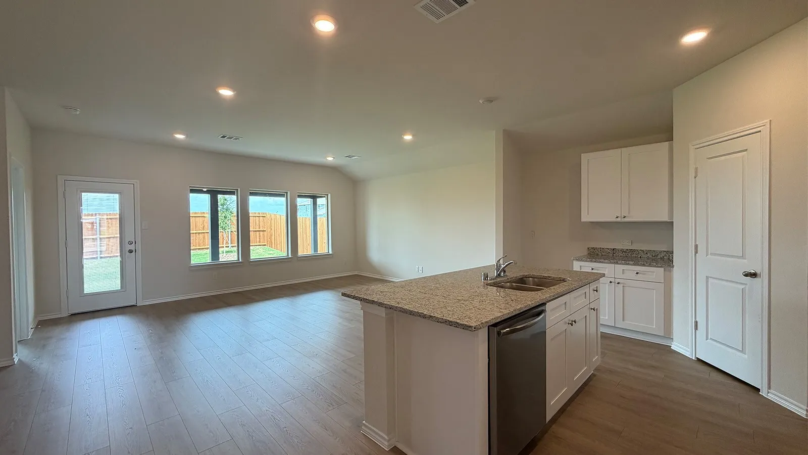 Open-concept living area featuring wood-finish flooring, recessed lighting, and a kitchen island with a double basin sink and stainless steel dishwasher