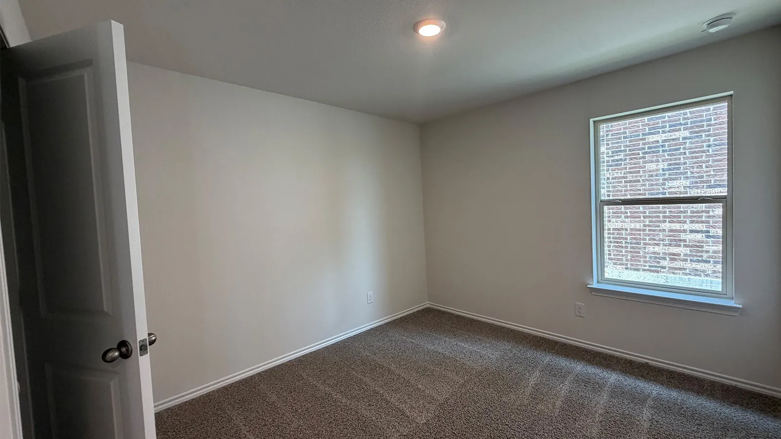 Carpeted room featuring a single window with white trim, a recessed ceiling light, and a white interior door with a dark handle