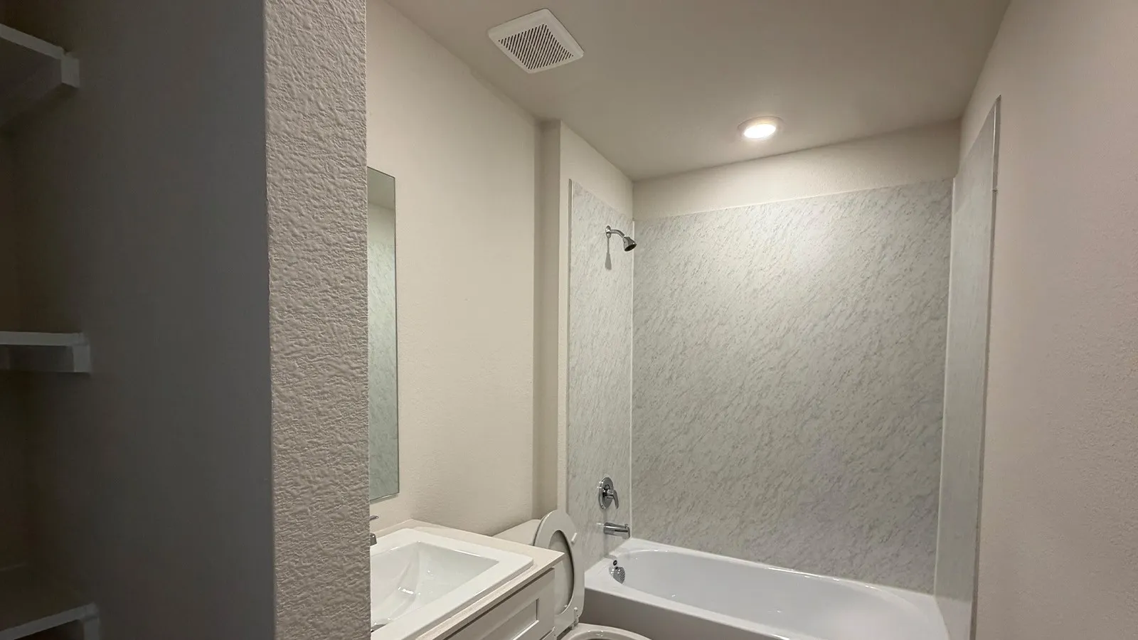 White tub and shower combination with textured wall surround, chrome fixtures, and recessed lighting