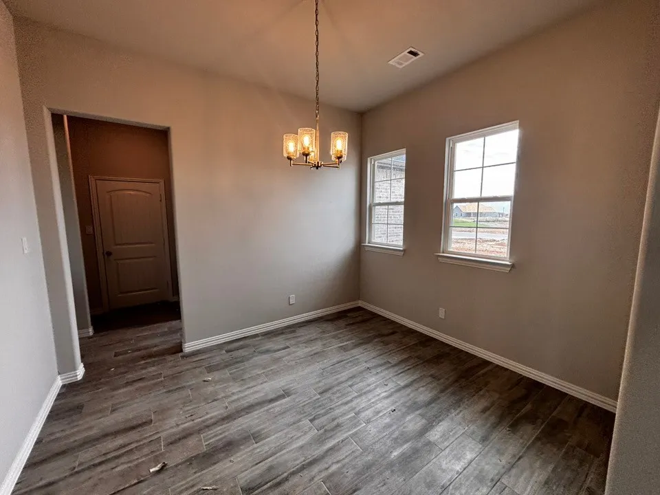 Wood-finish flooring, two large windows, overhead chandelier lighting, and a neutral wall palette