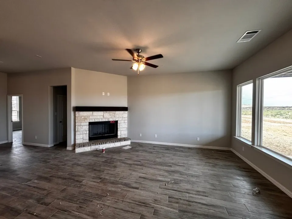 Spacious living area featuring wood-finish flooring, a stone-faced fireplace with a dark wood mantel, and a ceiling fan with integrated lighting
