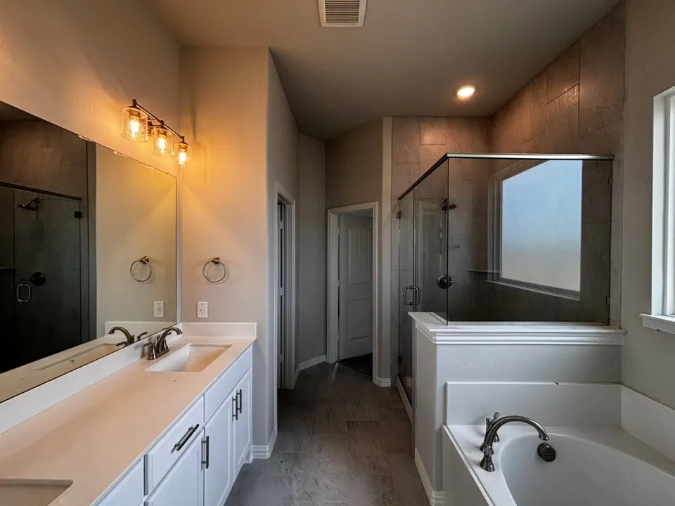 Dual vanity with white cabinetry, a spacious soaking tub, glass-enclosed shower with tiled walls, and recessed lighting