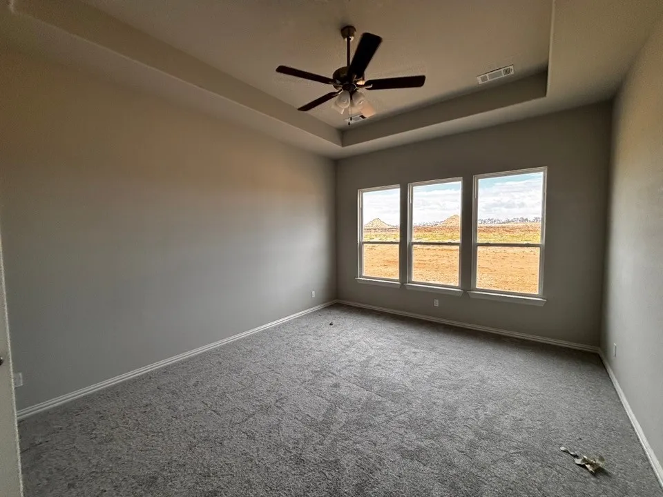 Tray ceiling with a ceiling fan, three pane windows, and gray carpeting
