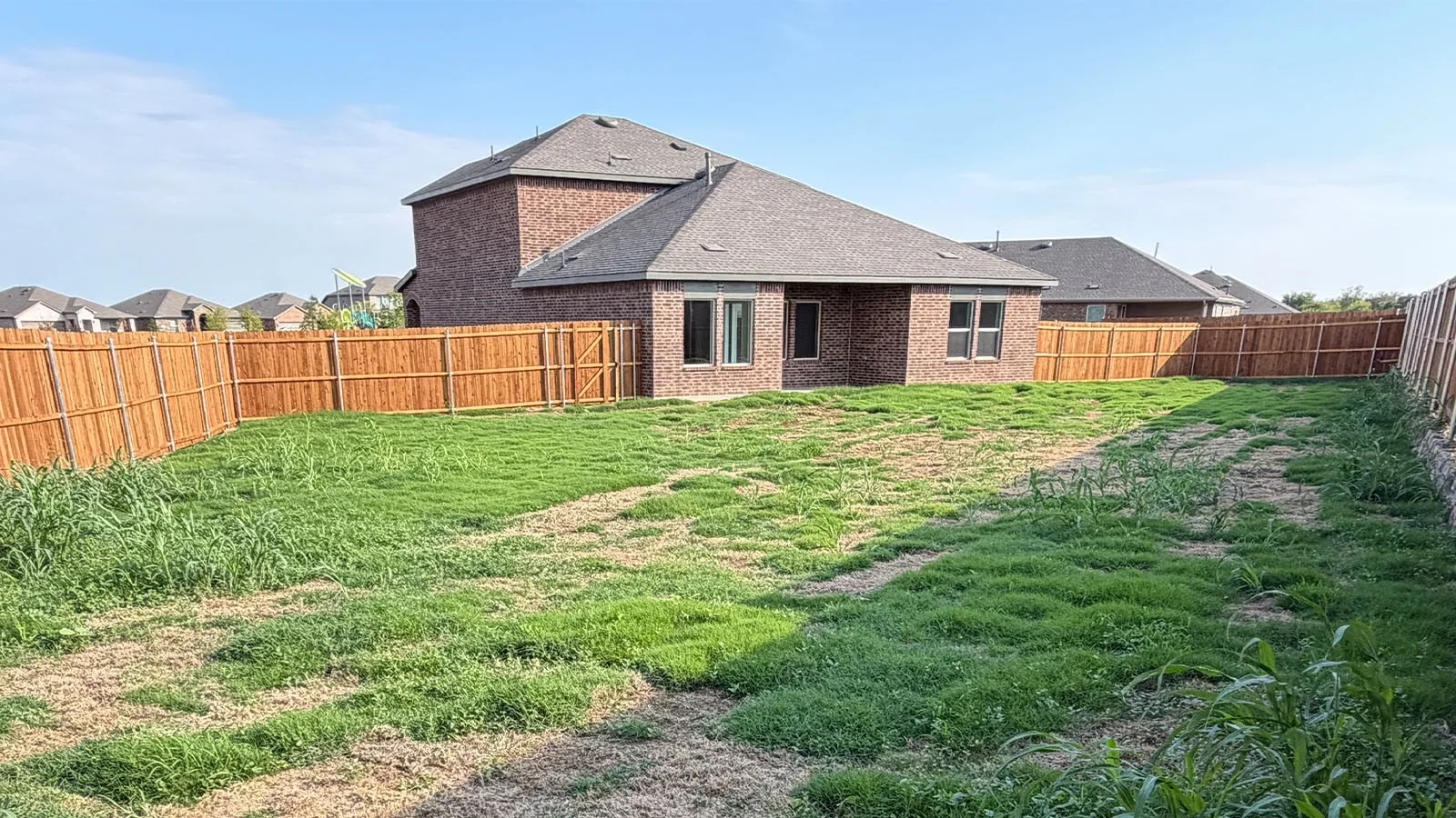 Expansive rear yard featuring a wooden privacy fence and brick exterior