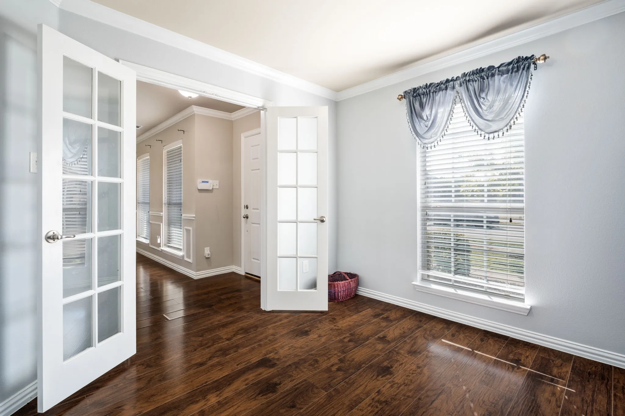 Wood-finish flooring, white French doors, crown molding, double window, and white trim