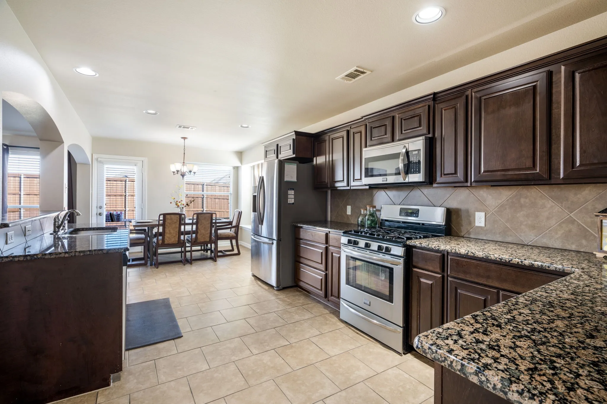 Kitchen featuring dark wood cabinetry, stainless steel appliances, granite-style countertops, and a tiled backsplash