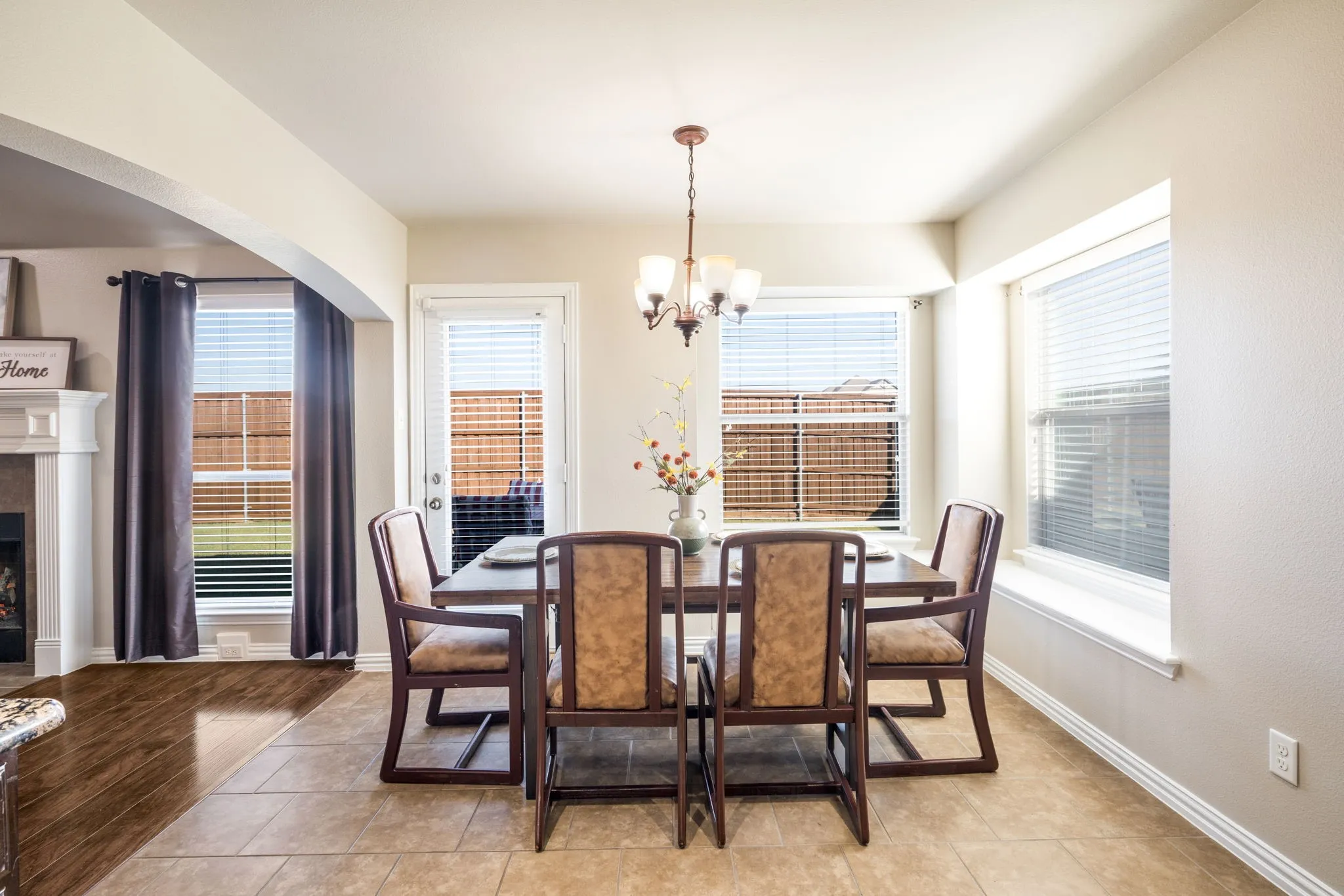 Tiled flooring in dining area with multiple windows, leading to an arched entryway and wood-finish flooring