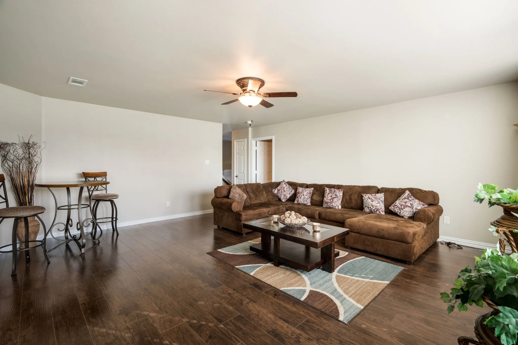 Spacious room with dark wood-finish flooring, light-toned walls, and a ceiling fan with integrated lighting