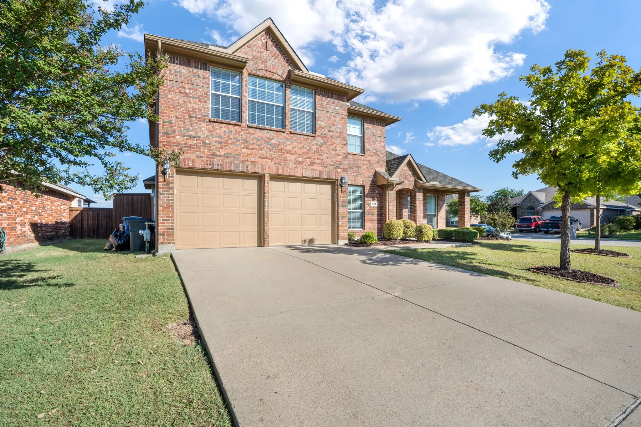 Brick exterior construction featuring a two-car garage, concrete driveway, and mature landscaping