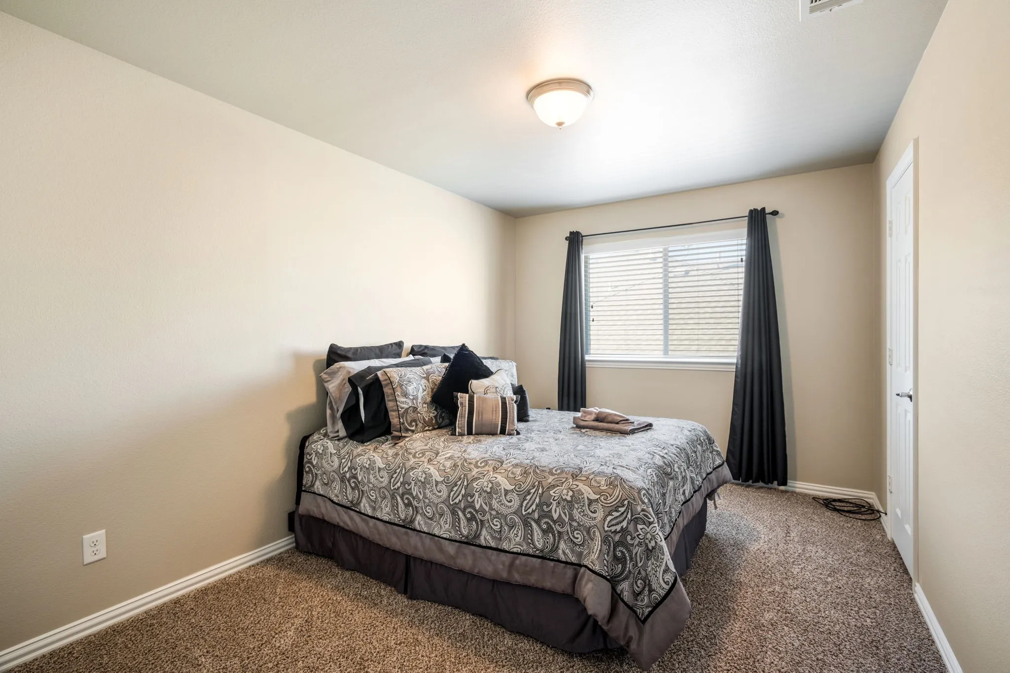 Wall-to-wall carpeting in a neutral tone, ceiling-mounted light fixture, and a window with blinds
