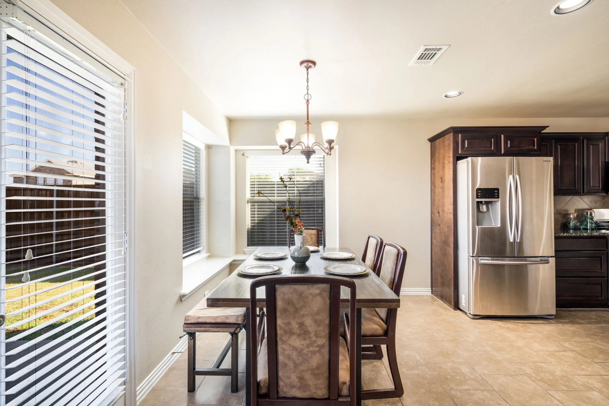Recessed lighting, tiled flooring, built-in dark wood cabinetry, stainless steel refrigerator, and a multi-light chandelier