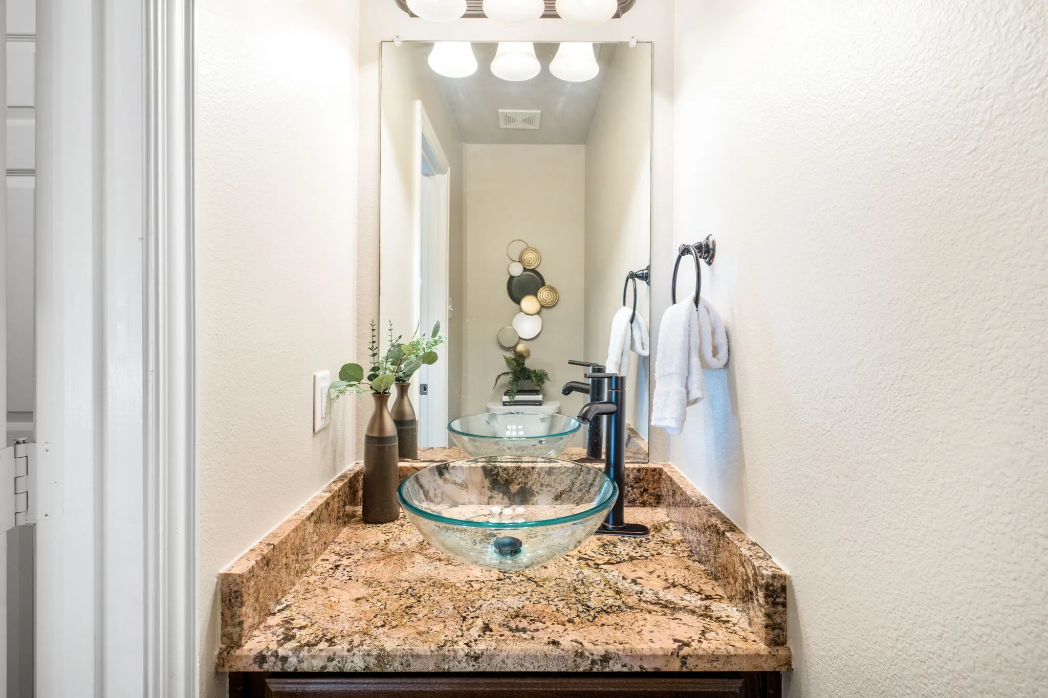 Vanity with a glass vessel sink, dark bronze faucet, and granite countertop