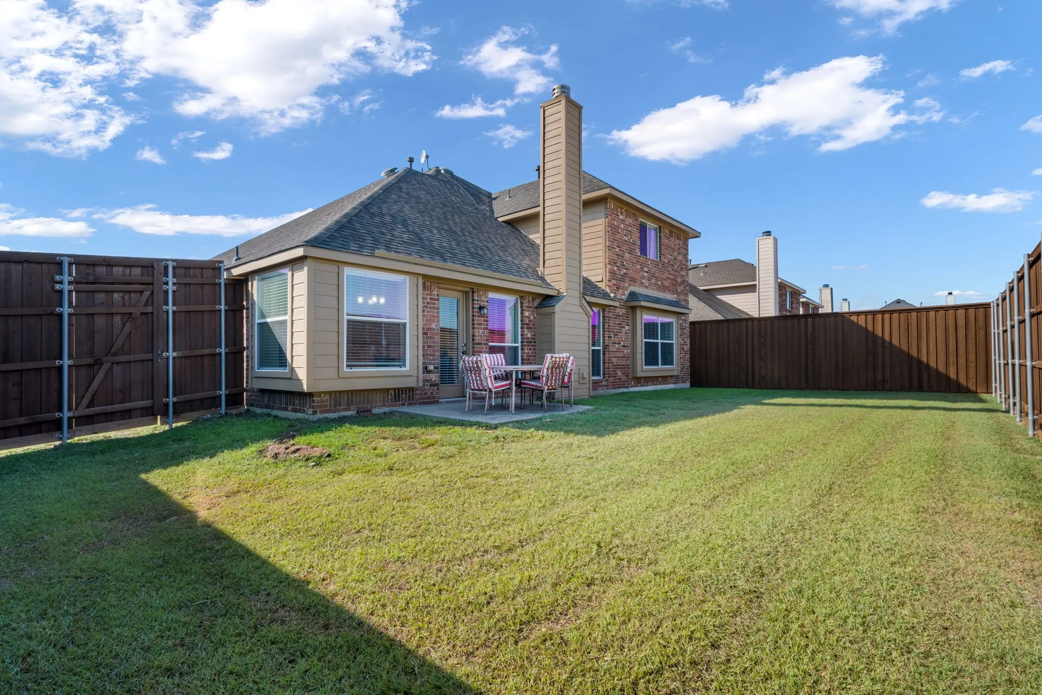 Expansive backyard featuring a manicured lawn, full privacy fencing, a brick exterior, and a rear patio