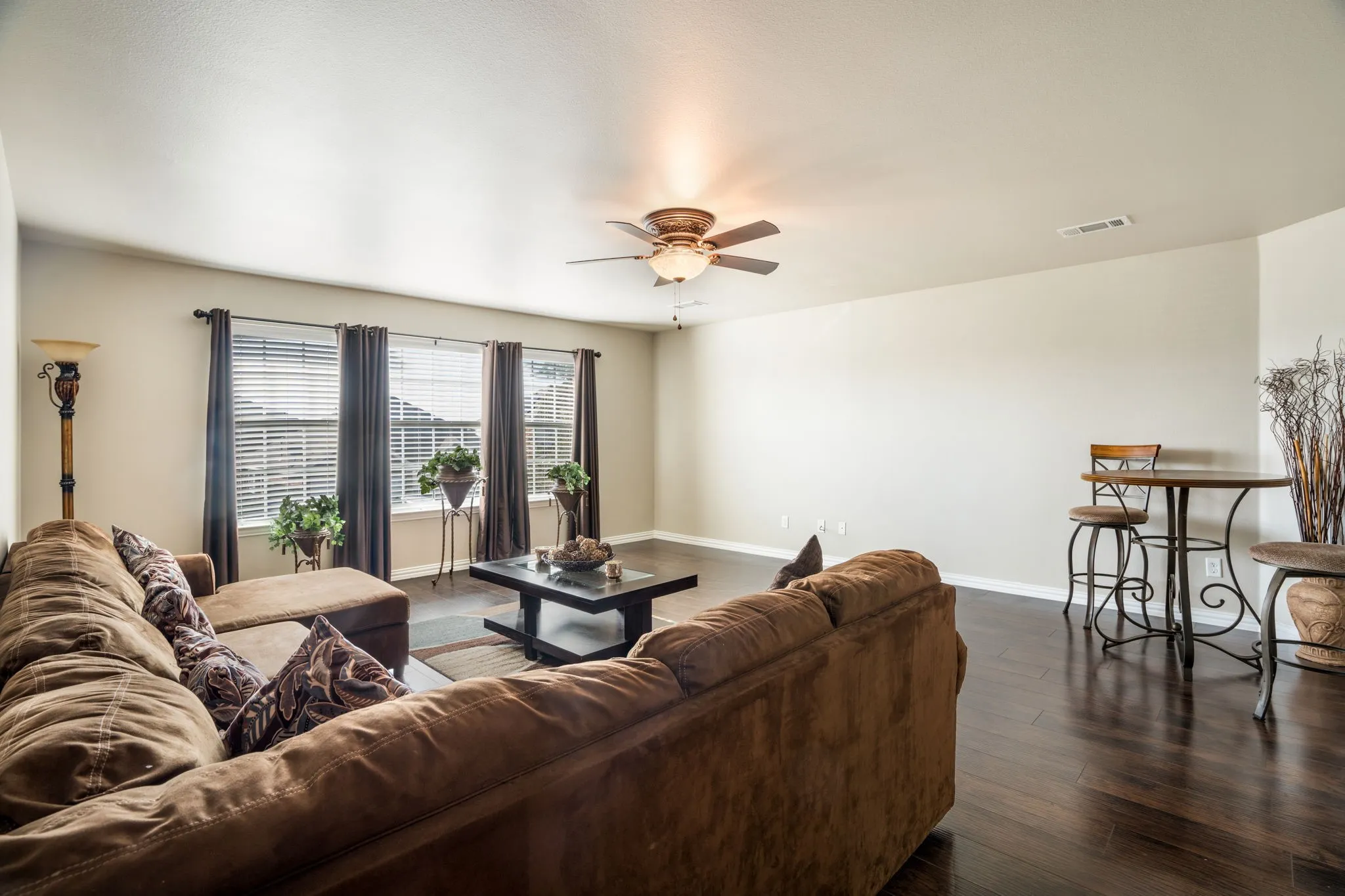 Dark wood-finish flooring throughout, ceiling fan with integrated lighting, multiple windows with blinds, ample wall space