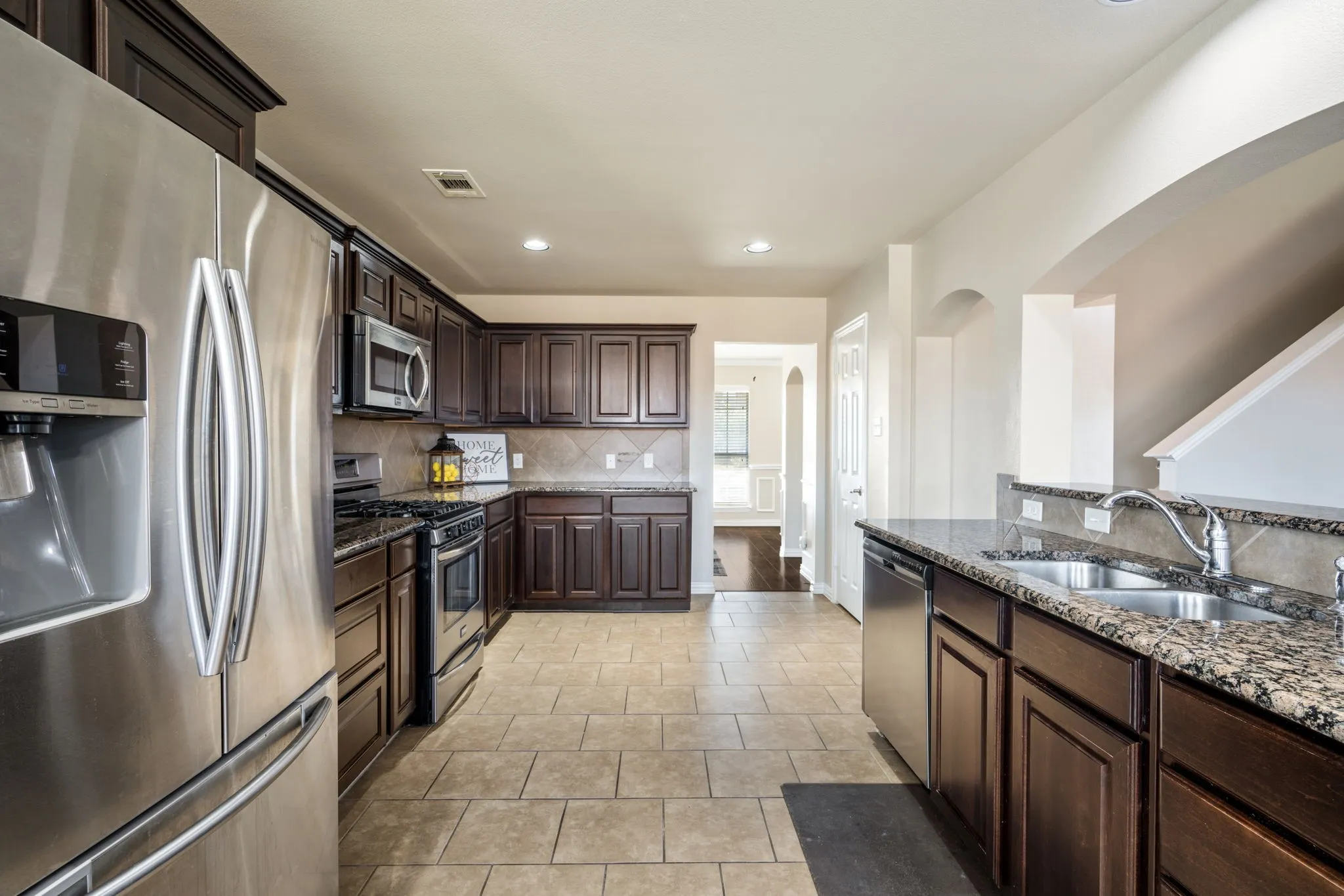 Kitchen featuring dark wood-finish cabinetry, stainless steel appliances, tiled backsplash, and granite countertops