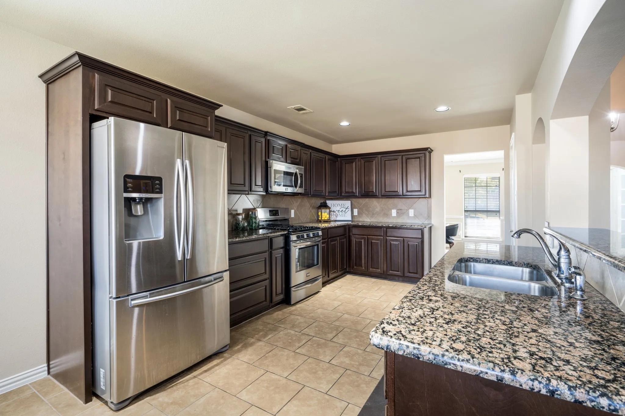 Spacious kitchen featuring dark wood cabinetry, stainless steel appliances, granite countertops, and a tiled backsplash