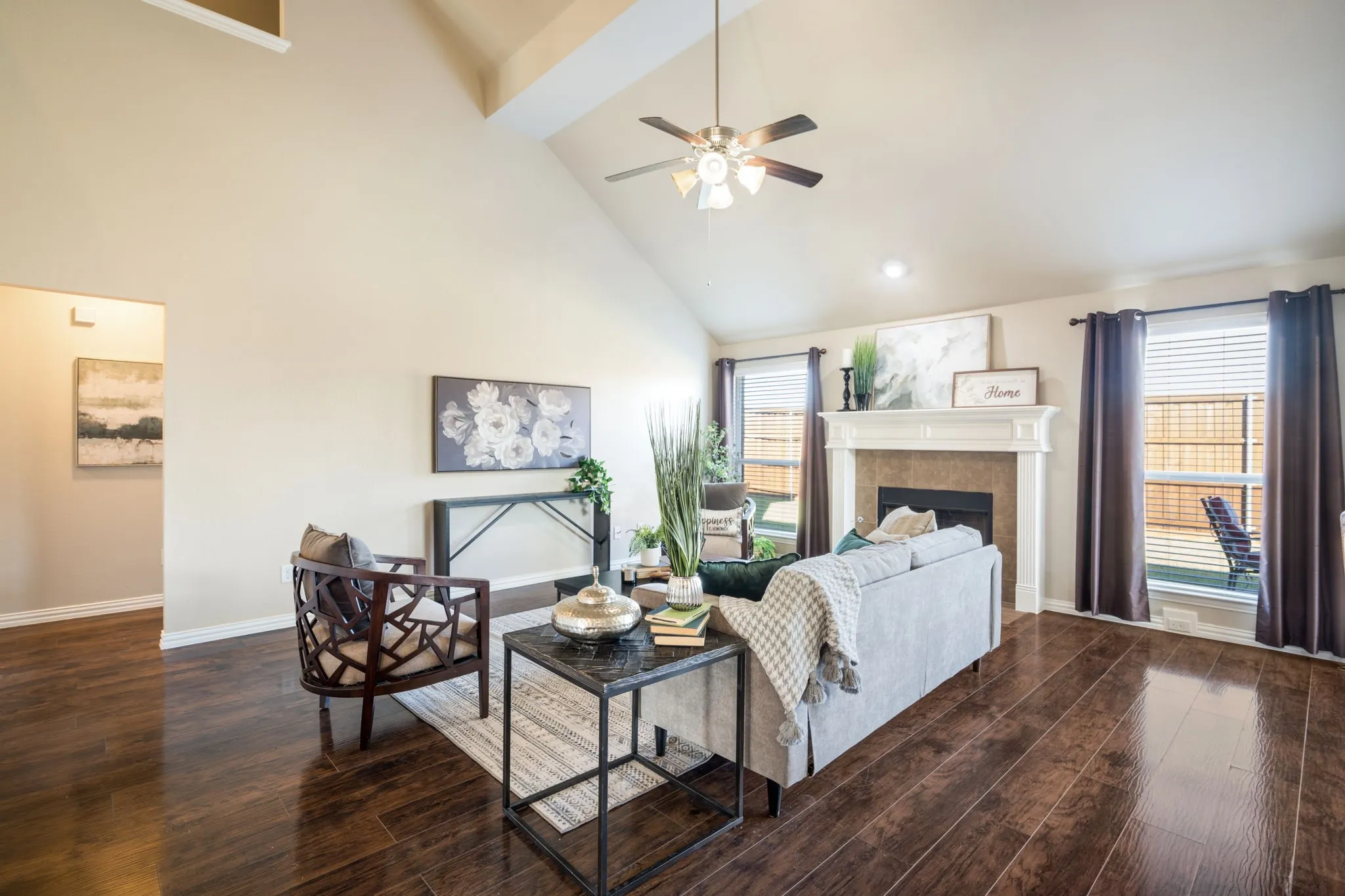 Vaulted ceiling with an attached ceiling fan, rich wood-finish flooring, fireplace with a white mantel, and multiple windows