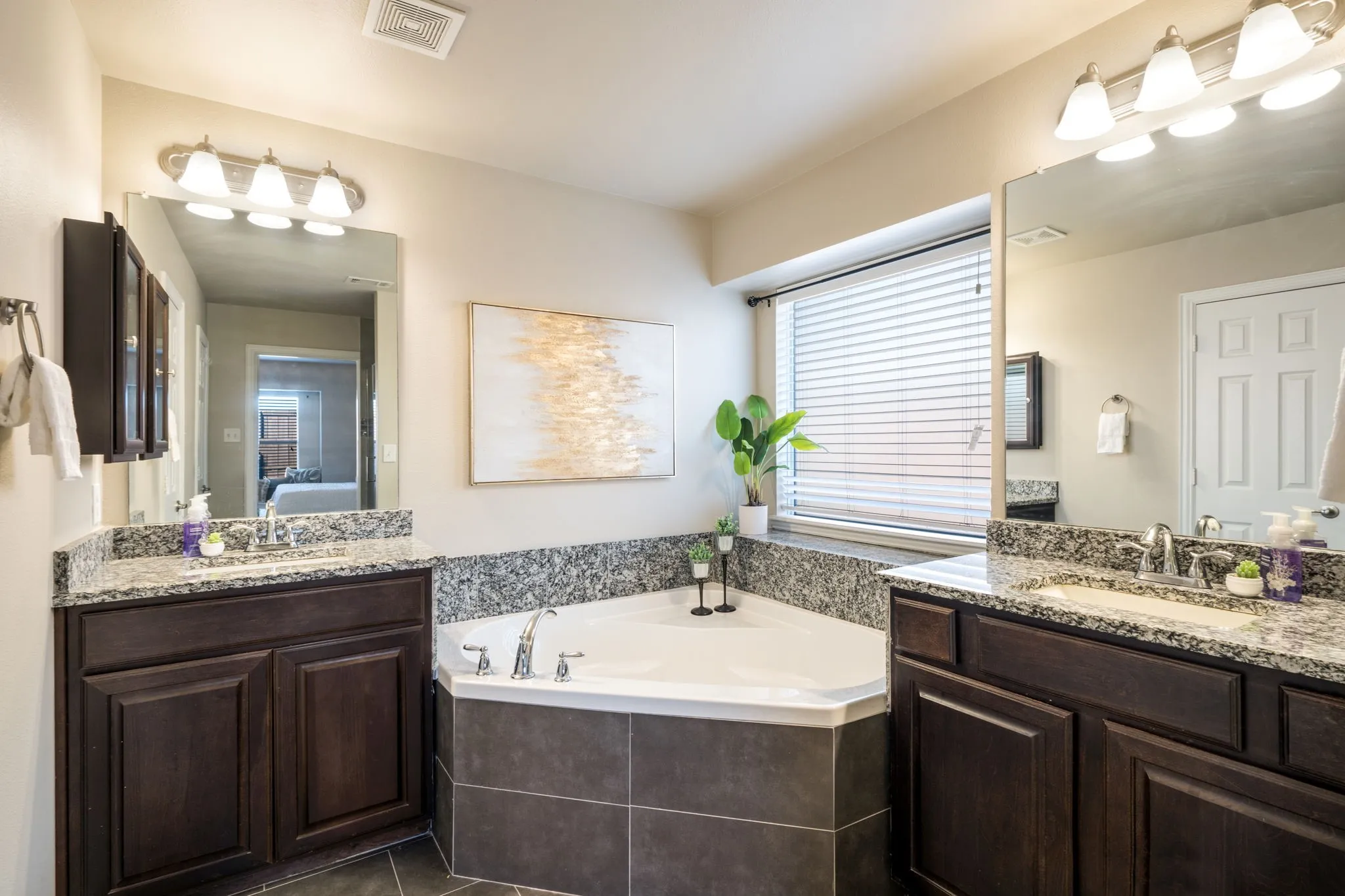 Dual dark wood vanities with granite countertops, undermount sinks, and chrome faucets flank a corner soaking tub