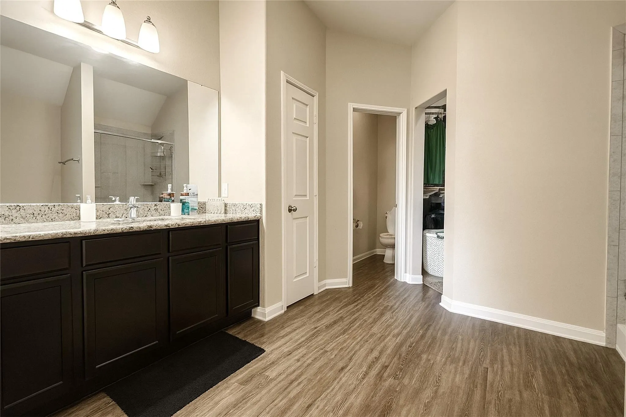 Dual vanity with granite-style countertop, dark wood-finish cabinetry, and wood-finish flooring