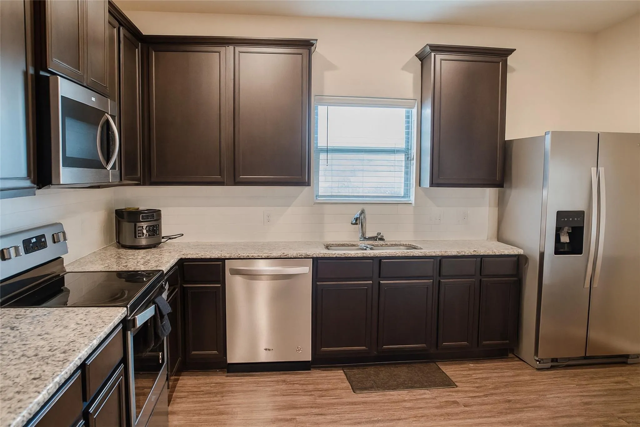 Kitchen featuring dark wood-finish cabinetry, light-toned countertops, a stainless steel sink with a chrome faucet, and stainless steel appliances